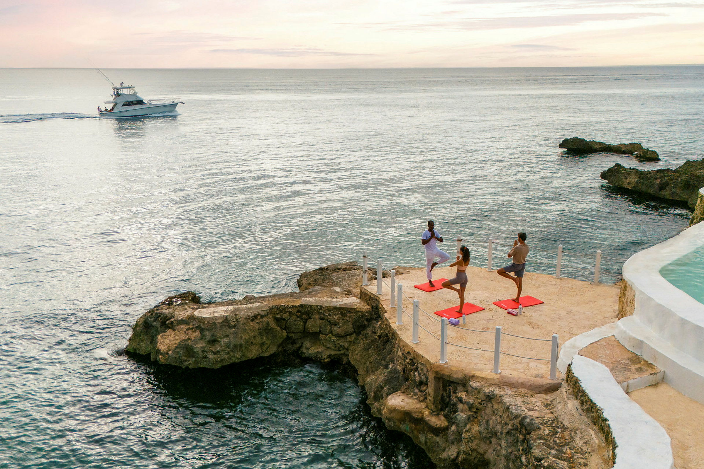 Personer som driver med yoga ved sjøen på et steinete klippe, med en båt på vannet i bakgrunnen. (AI-generert tekst)