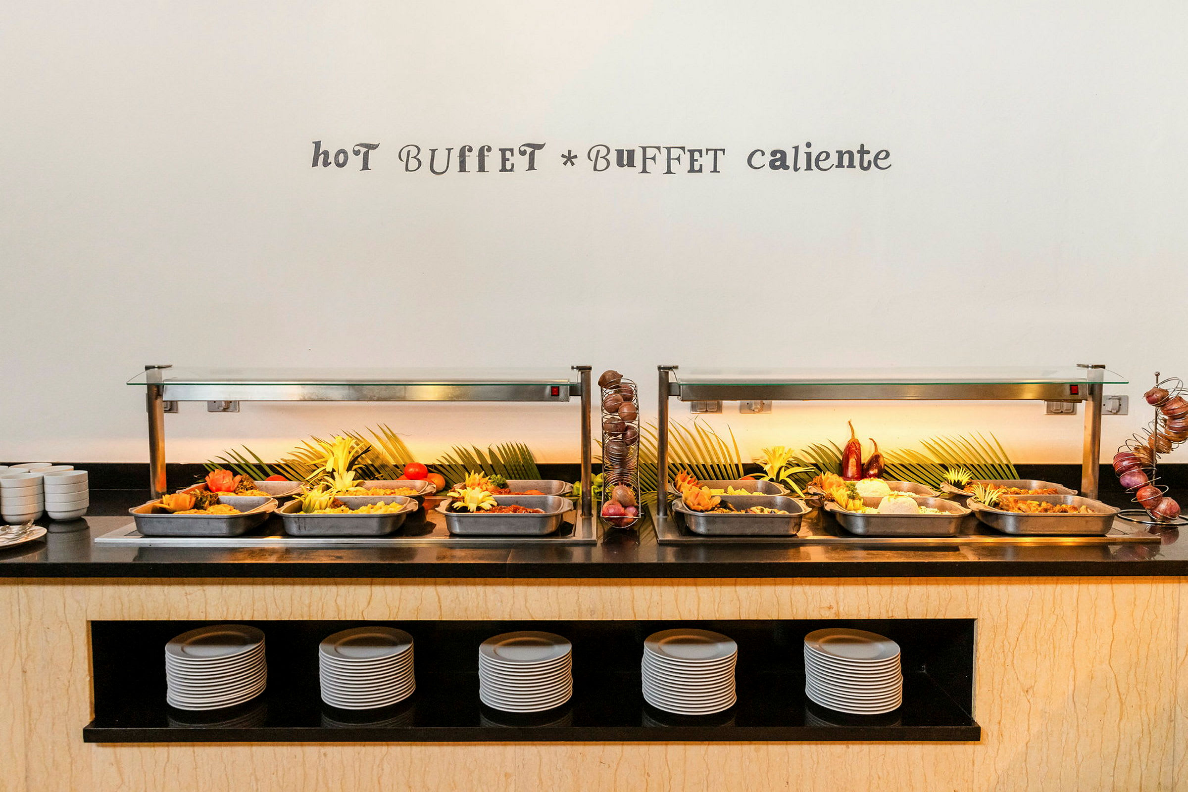 Et varmt buffetbord med ulike retter servert i stålformer, dekorert med grønne blader og frisk grønnsaker. (AI-generert tekst)