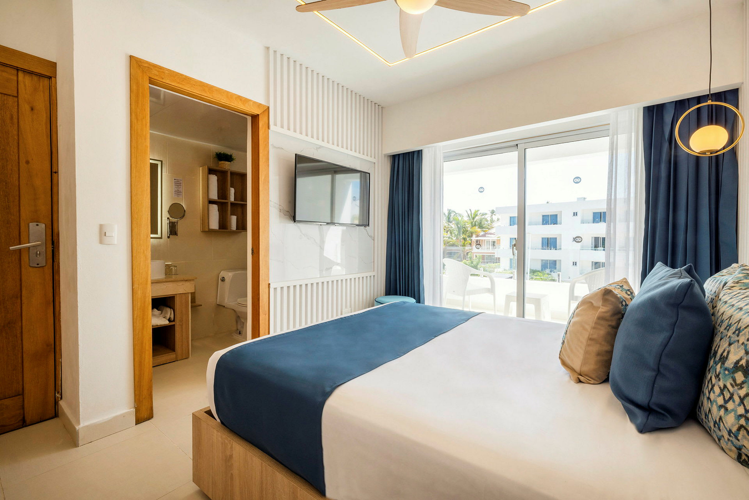 Et moderne hotellrom med dobbeltseng, bad ved siden av til venstre og vinduer ut mot en balkong. (AI-generert tekst)