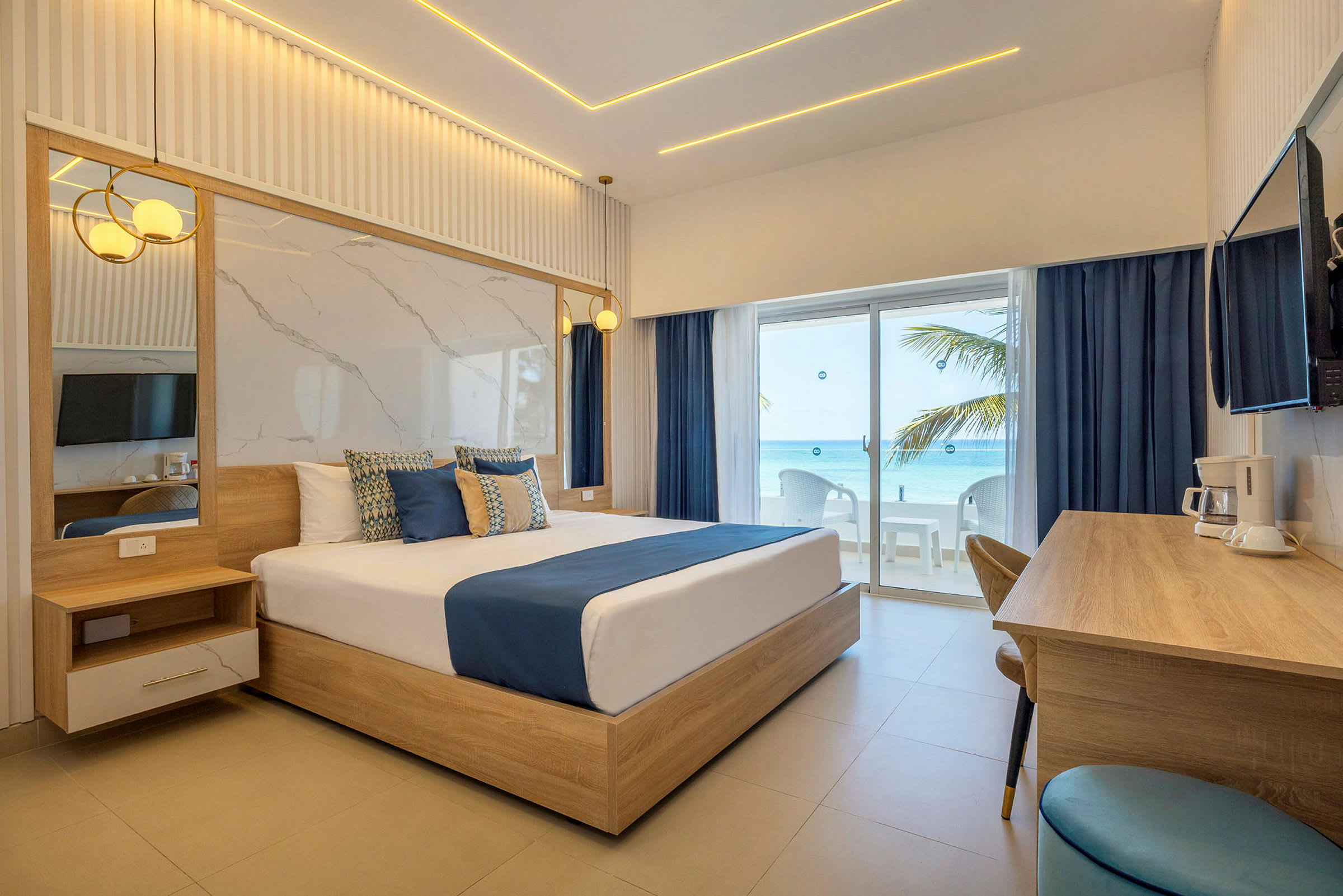 Et stilig hotellrom med en stor seng, tremøbler og utsikt mot havet gjennom glassdører. (AI-generert tekst)