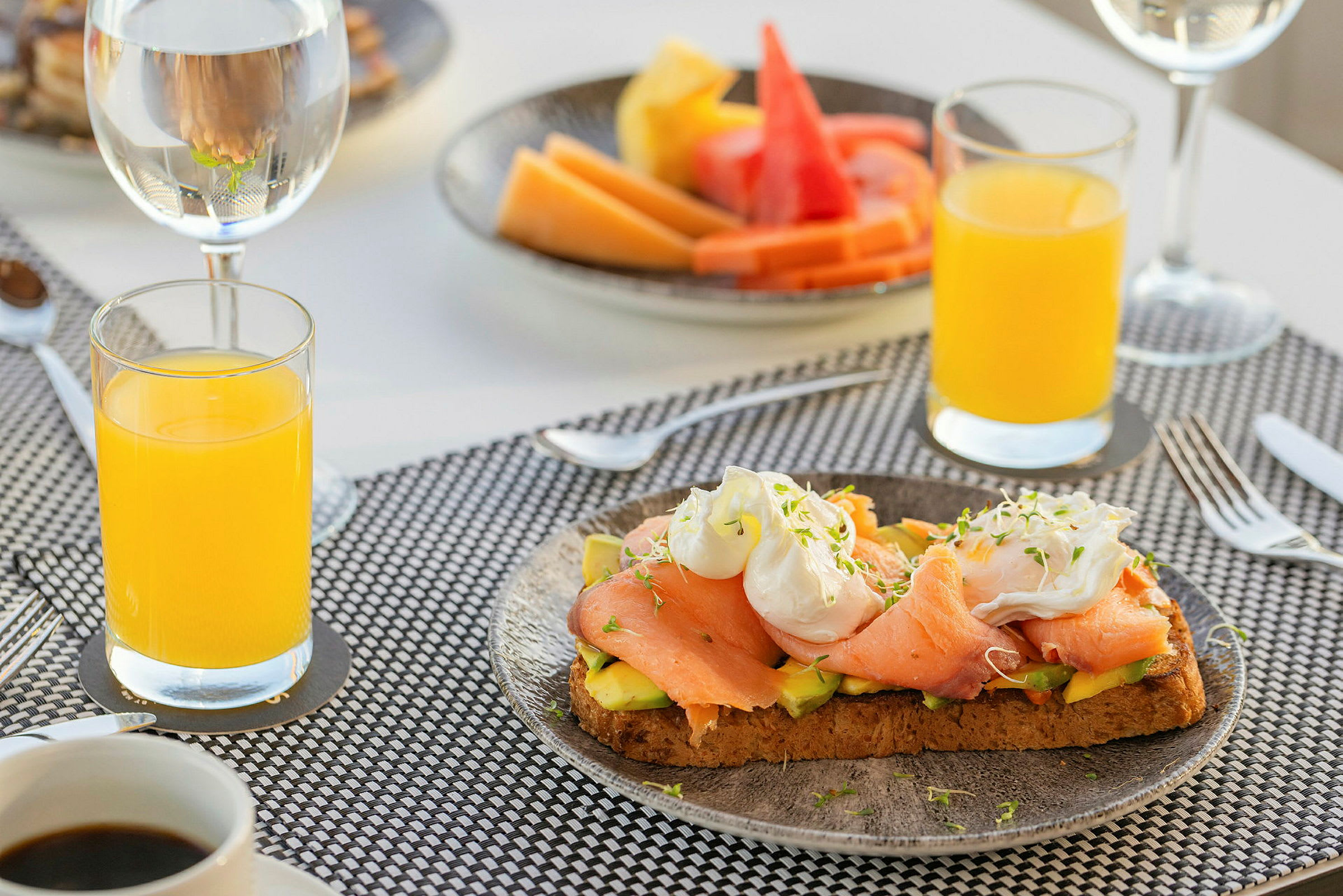 En frokost med juice, kaffe, toast med laks og avokado og en tallerken med frukt. (AI-generert tekst)