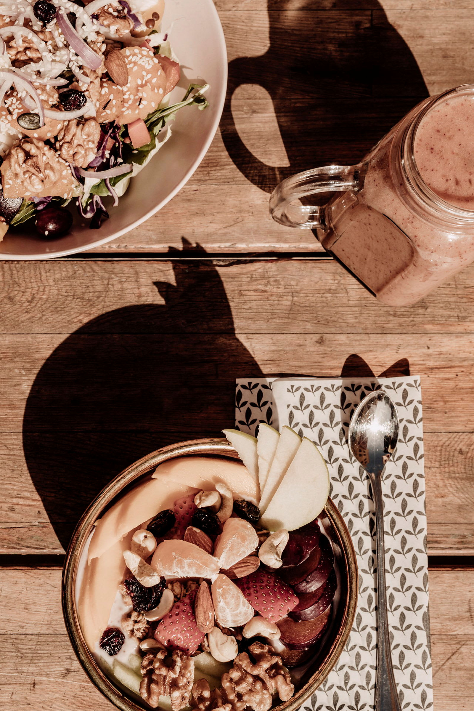 Et måltid med blandet salat og en bolle full av frukt og nøtter på et trebord. (AI-generert tekst)