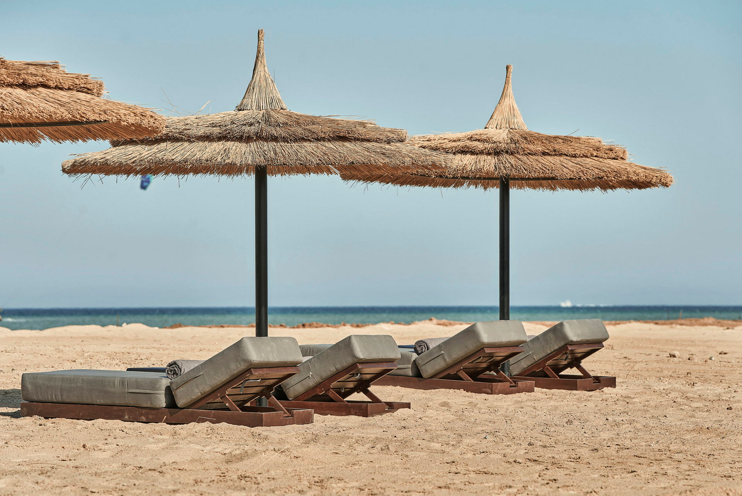 Solstoler med stråtak på sandstrand med hav i bakgrunnen. (AI-generert tekst)