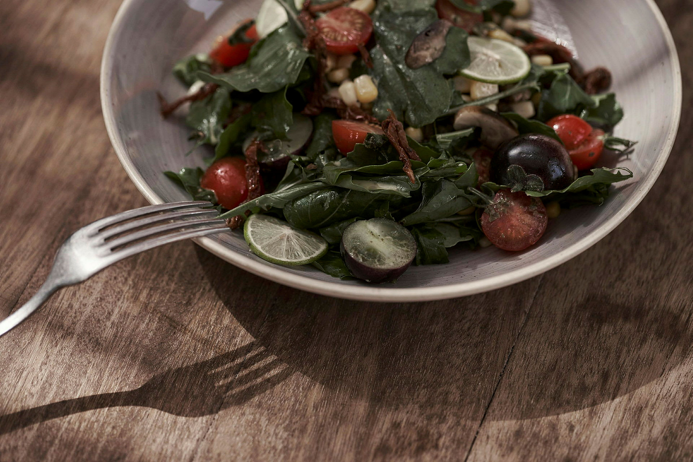 En salat med forskjellige grønnsaker og frukt servert på en tallerken med en gaffel ved siden av. (AI-generert tekst)
