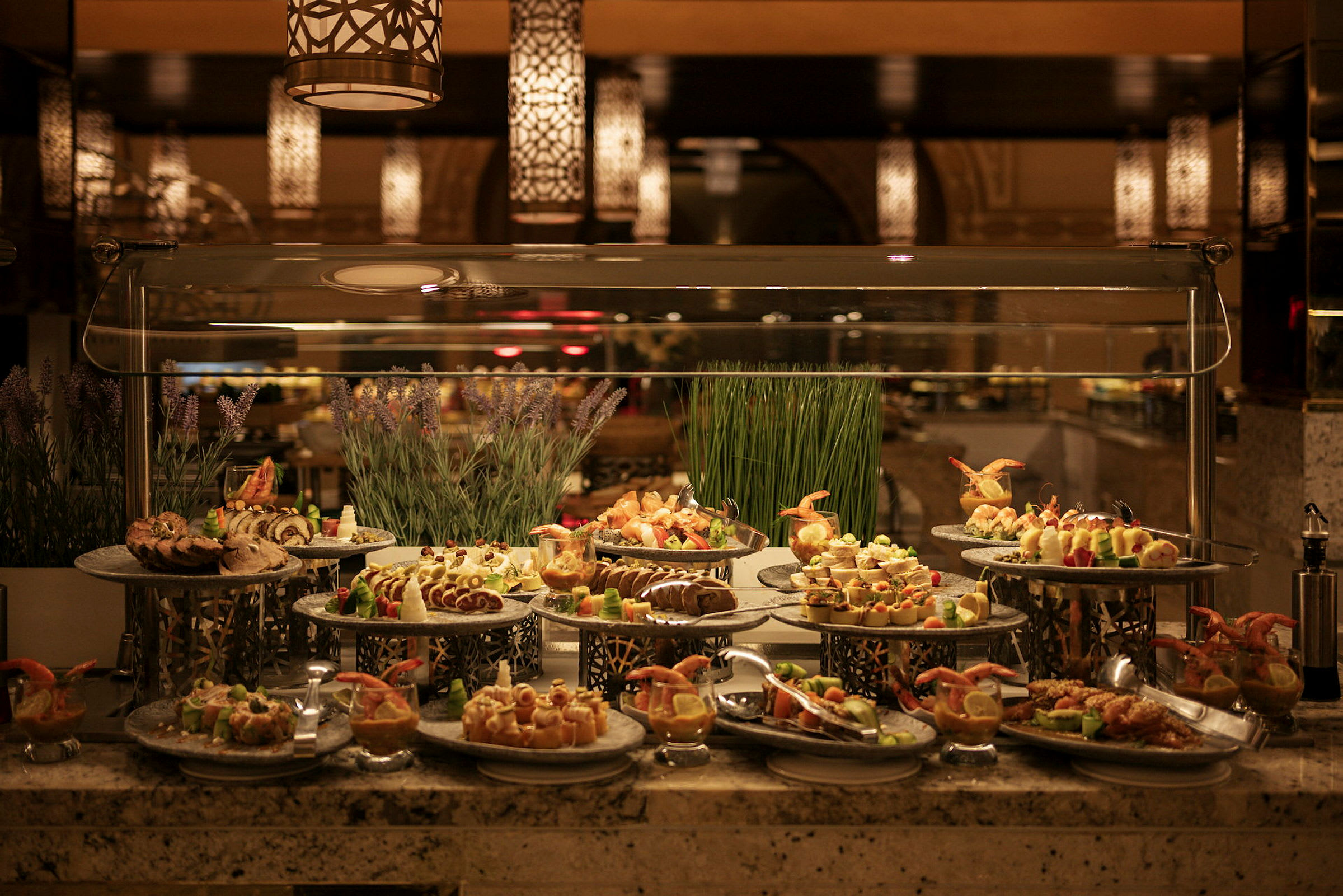 En buffet med forskjellige retter presentert på metallfat, dekorert med urter og gress. (AI-generert tekst)