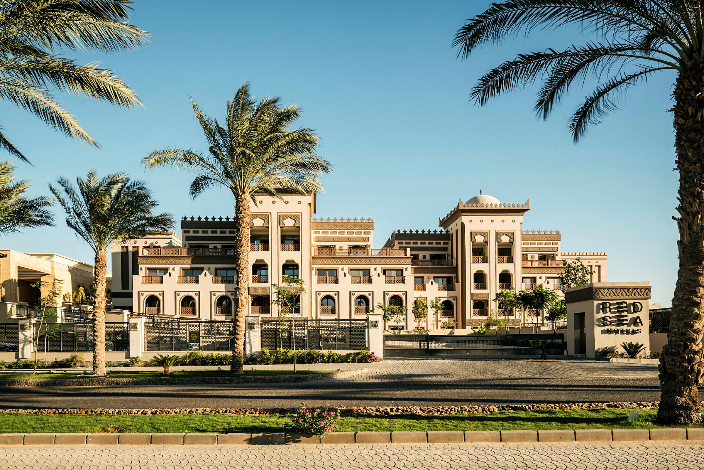Et elegant hotellkompleks i arabisk stil med palmer i forgrunnen under en klar blå himmel. (AI-generert tekst)
