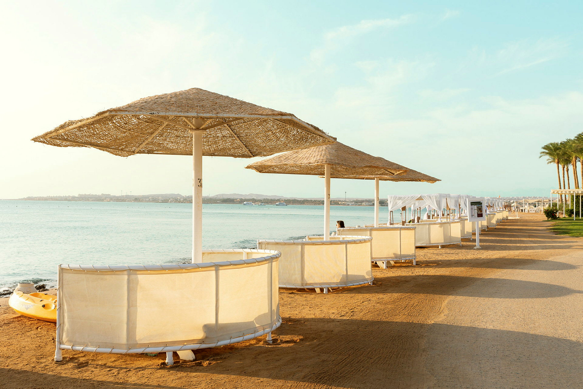 Strand med parasoller og solbåser ved vannet. (AI-generert tekst)