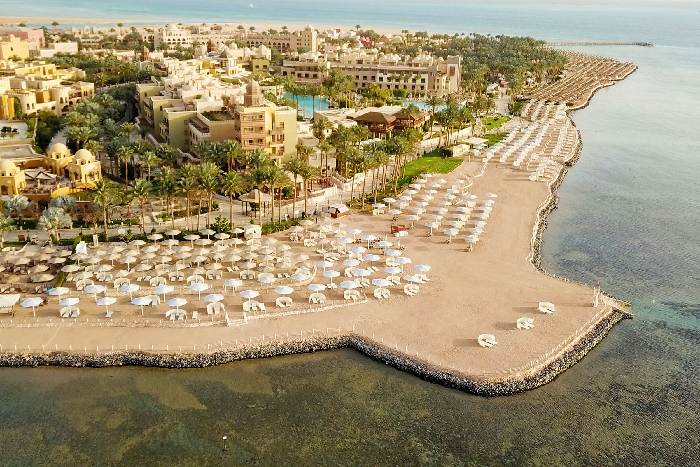 Luftfoto av en strand med parasoller og hotellbygninger i bakgrunnen. (AI-generert tekst)