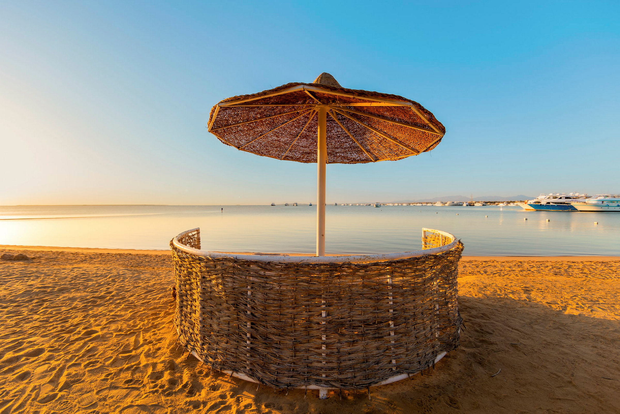 Strand med solskjerm av flettet materiale og havet i bakgrunnen. (AI-generert tekst)