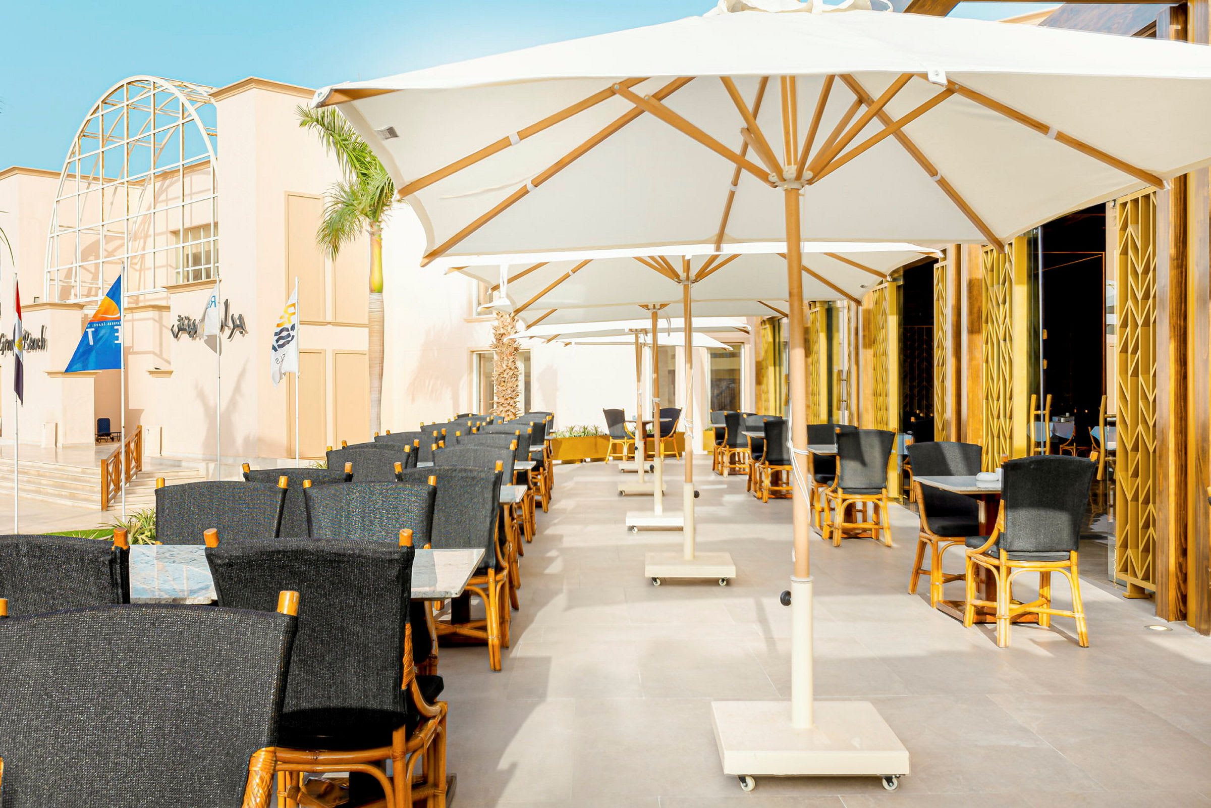 Utendørs restaurant med hvite parasoller og stoler av tre og mørkt stoff. (AI-generert tekst)