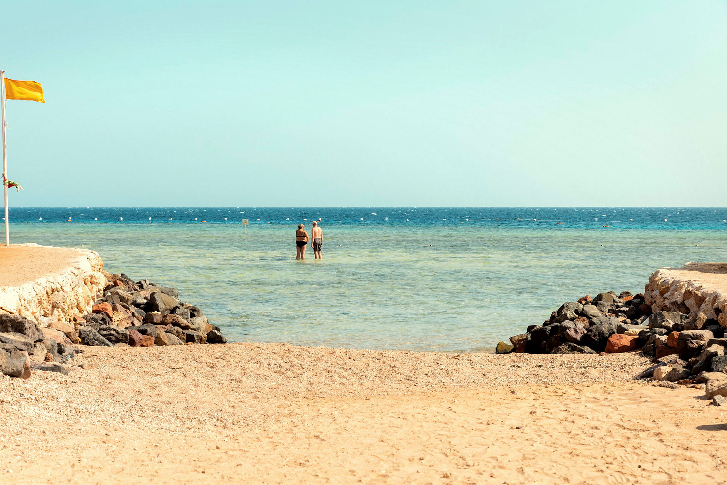 To personer står i grunt vann ved en strand. (AI-generert tekst)
