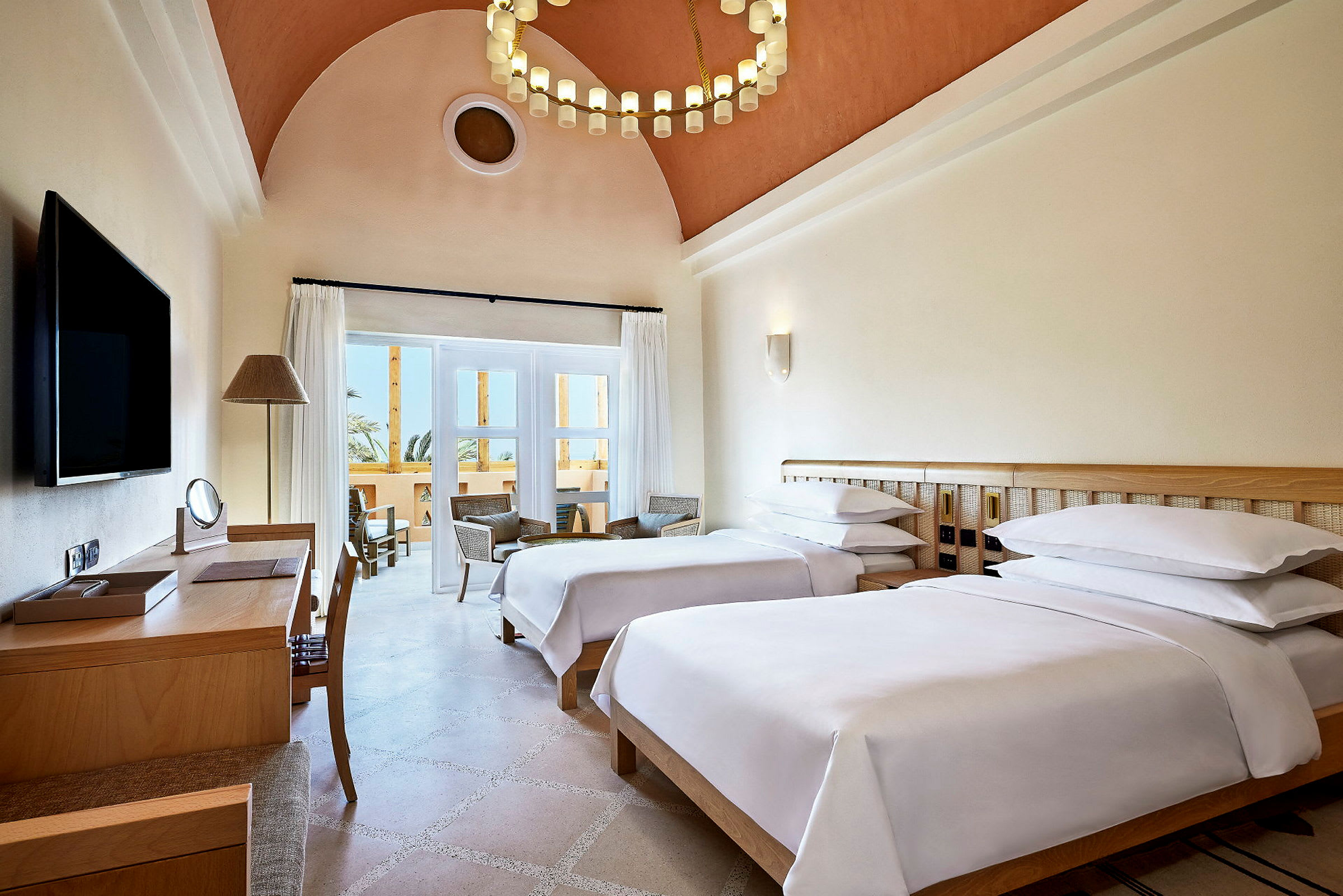 Hotellrom med to enkeltsenger, skrivebord og sittegruppe ved balkongen. (AI-generert tekst)