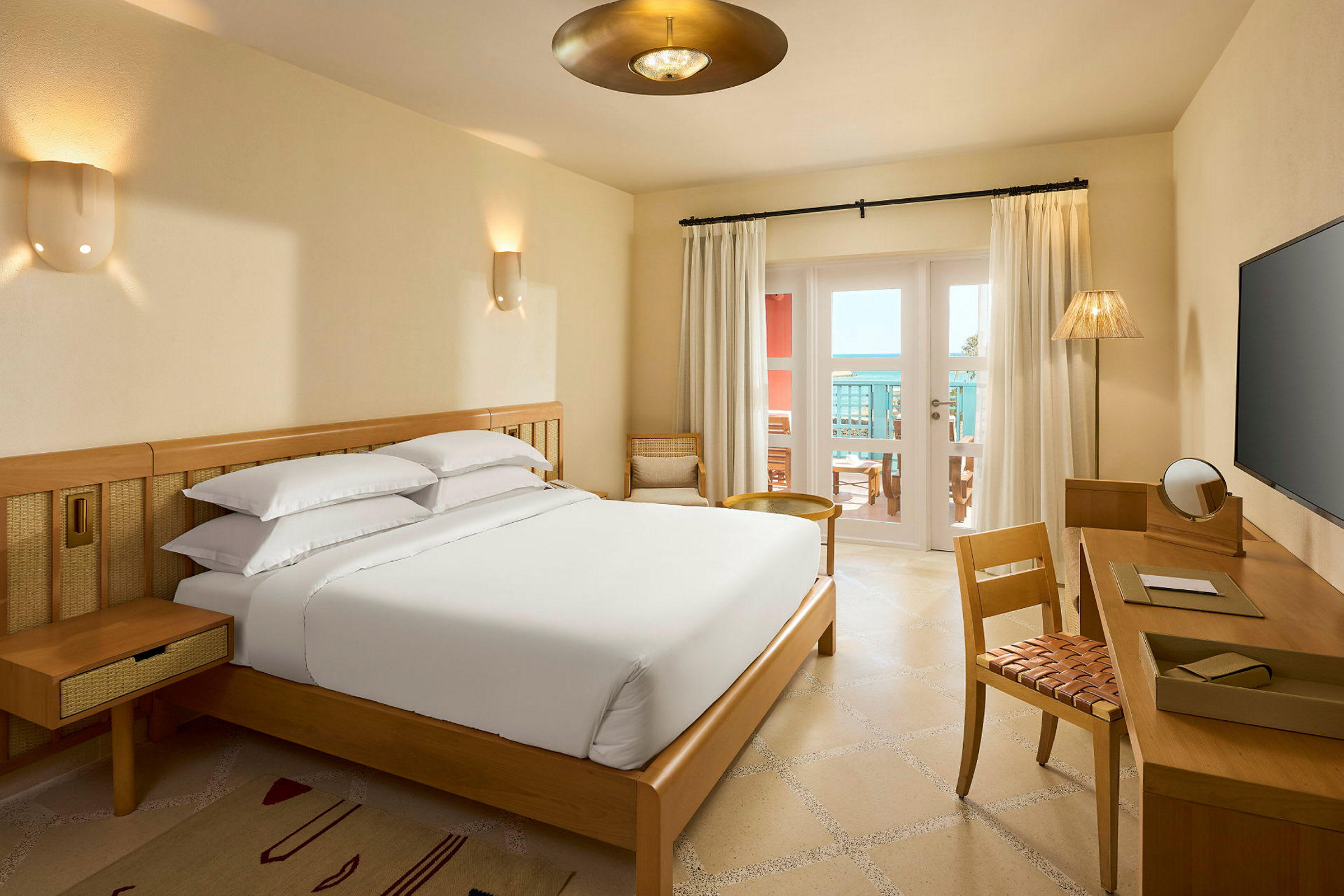 Et hotellrom med en seng, skrivebord og en balkong med utsikt. (AI-generert tekst)