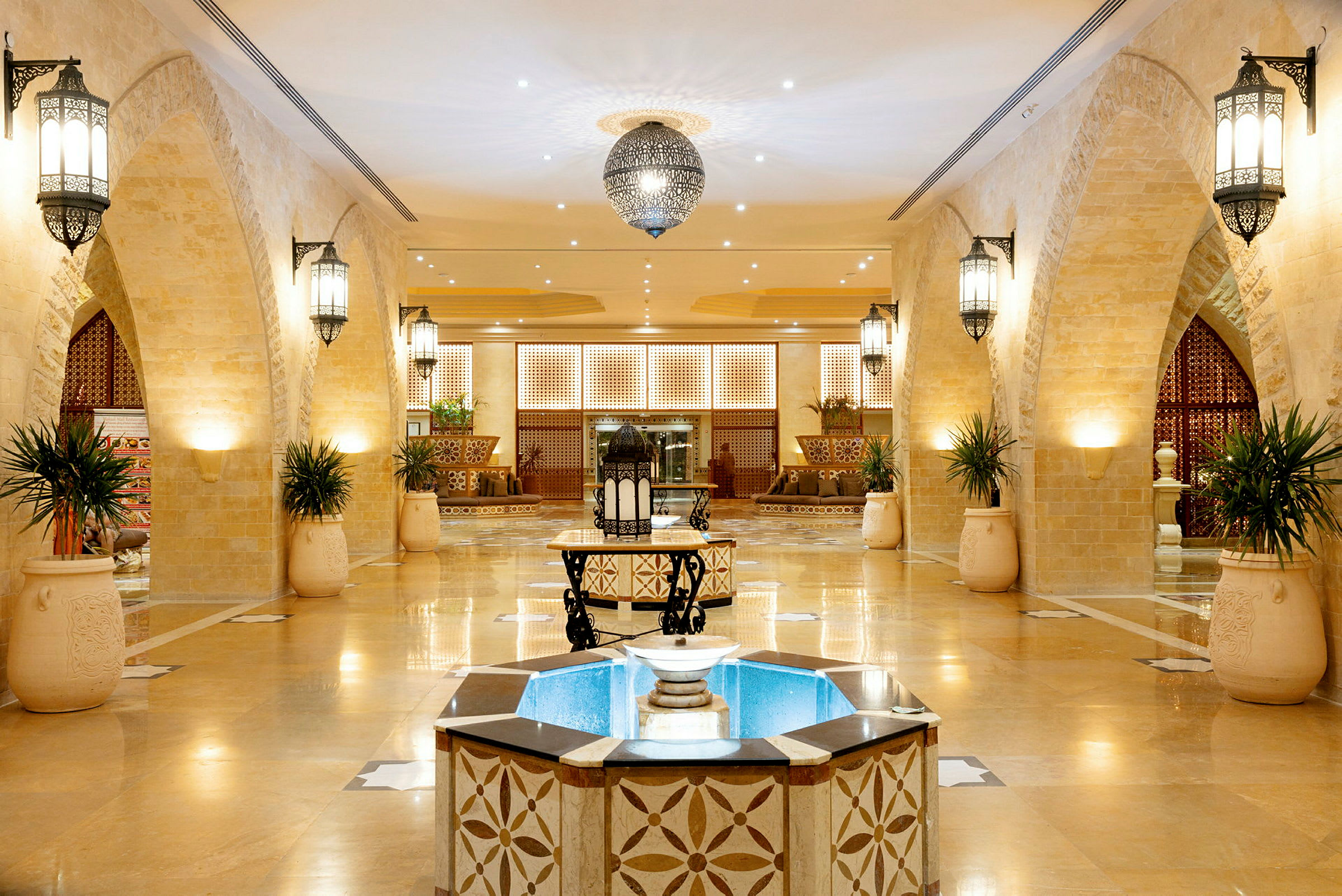 Hotellobby med lys innredning, ornamenterte buer og sentral fontene. (AI-generert tekst)