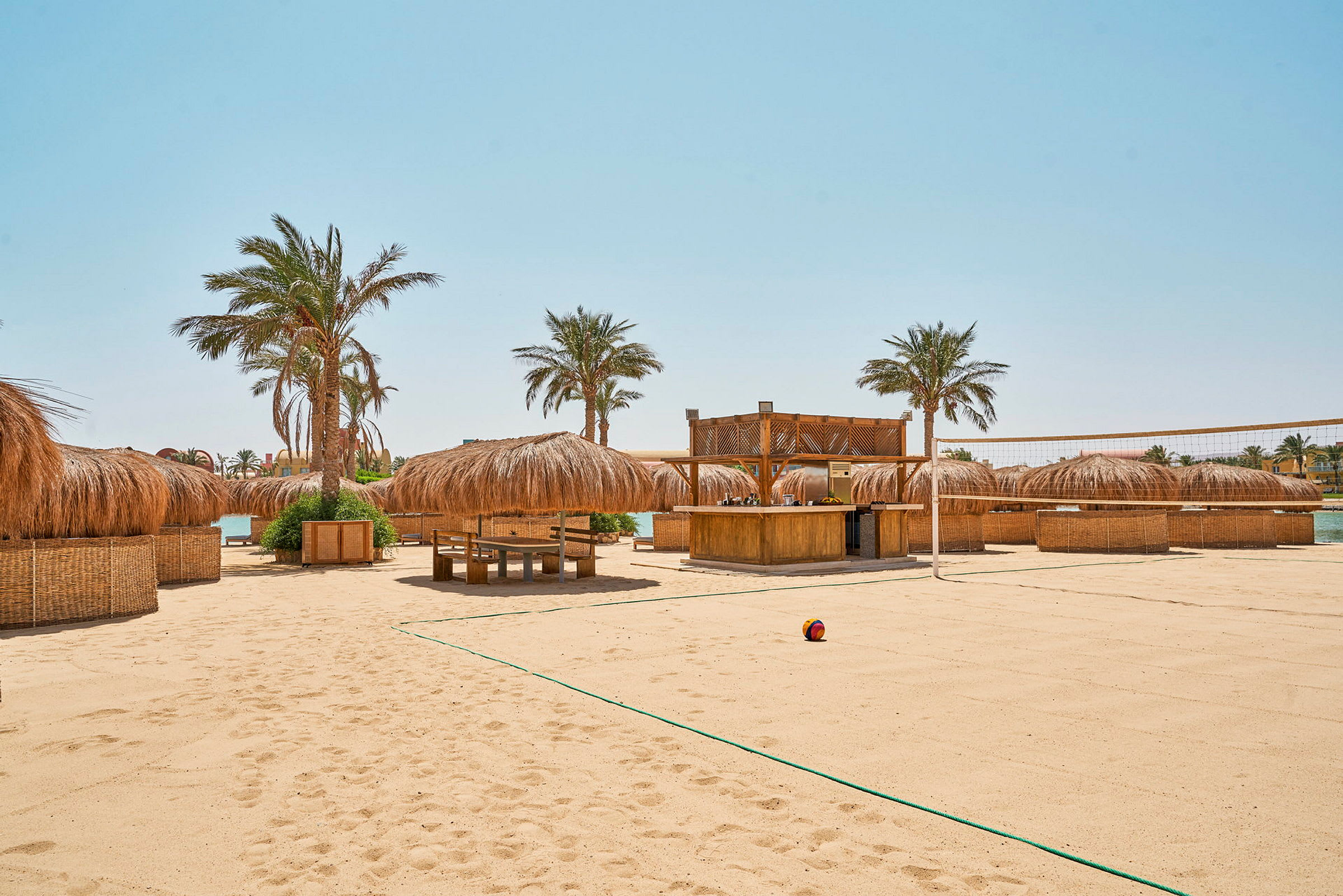 Strand med sand, palmer og parasoller samt en strandvolleyballbane. (AI-generert tekst)