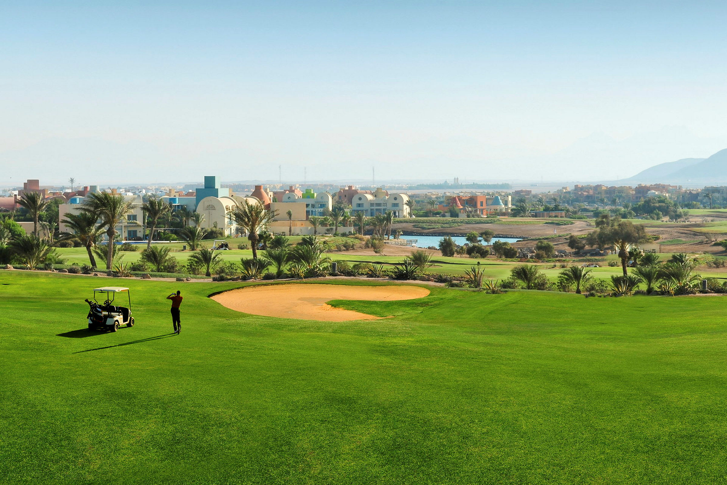 Grønn golfbane med en golfspiller og en golfbil i forgrunnen. (AI-generert tekst)