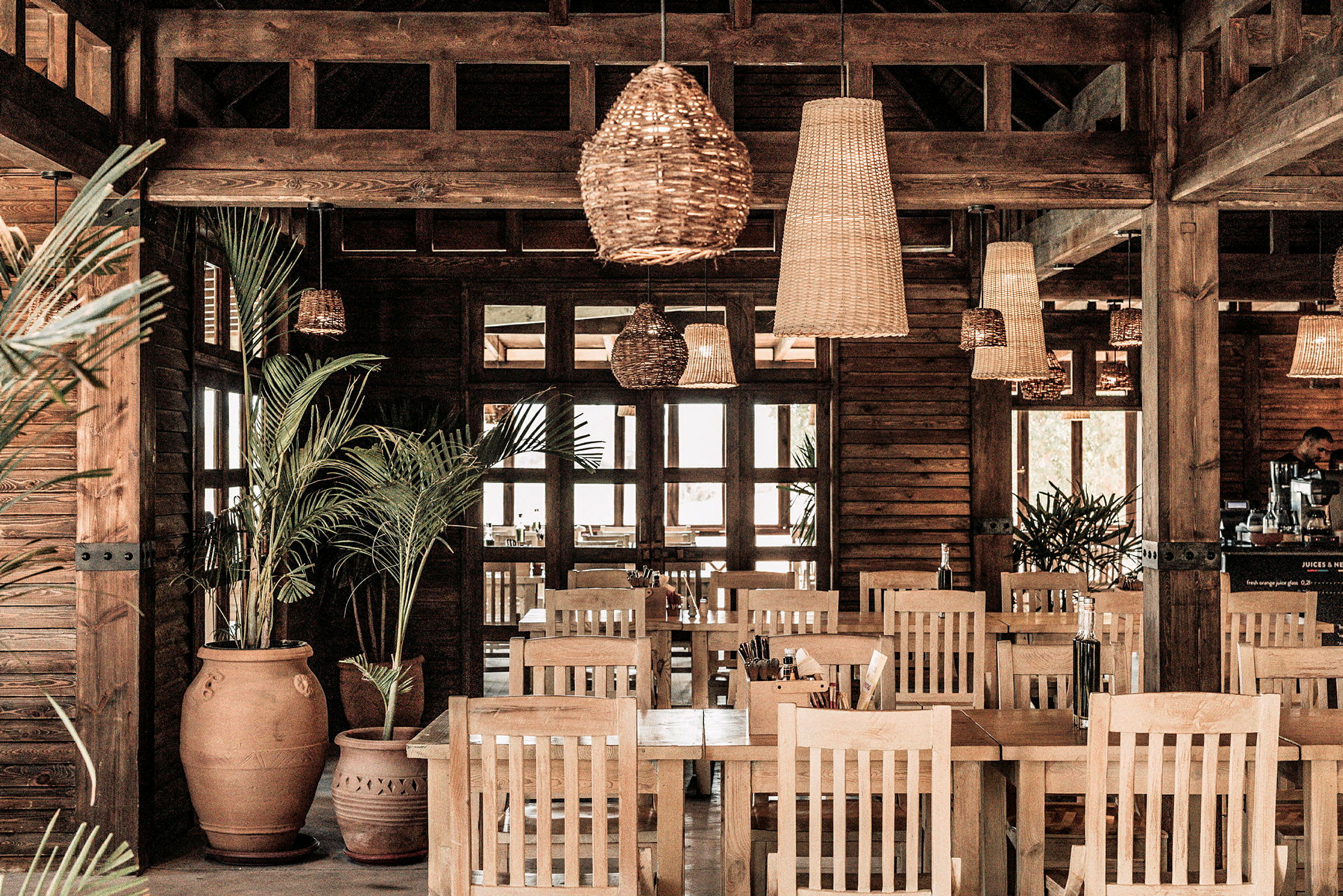 Interiør av en restaurant med tredetaljer, planter og rottinglamper. (AI-generert tekst)