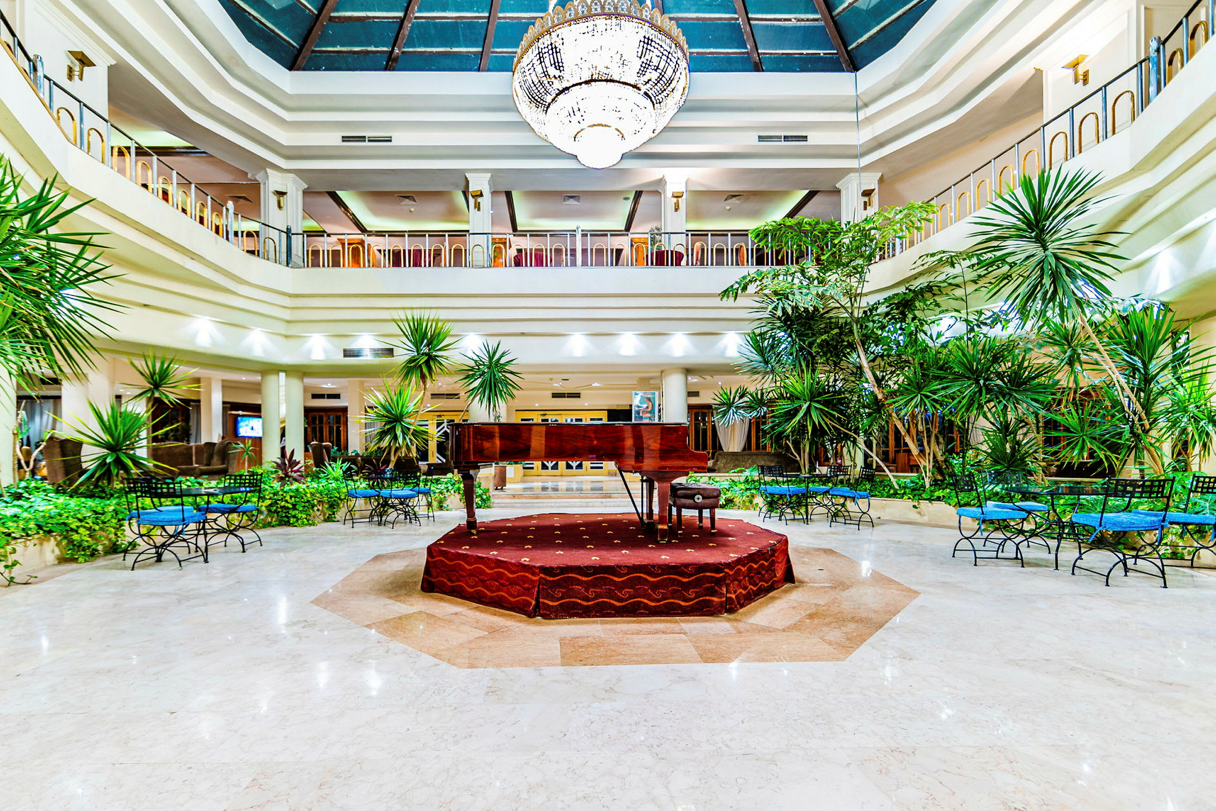 Et flygel plassert på en forhøyet scene i en romslig hotellobby med plantedekorasjoner. (AI-generert tekst)