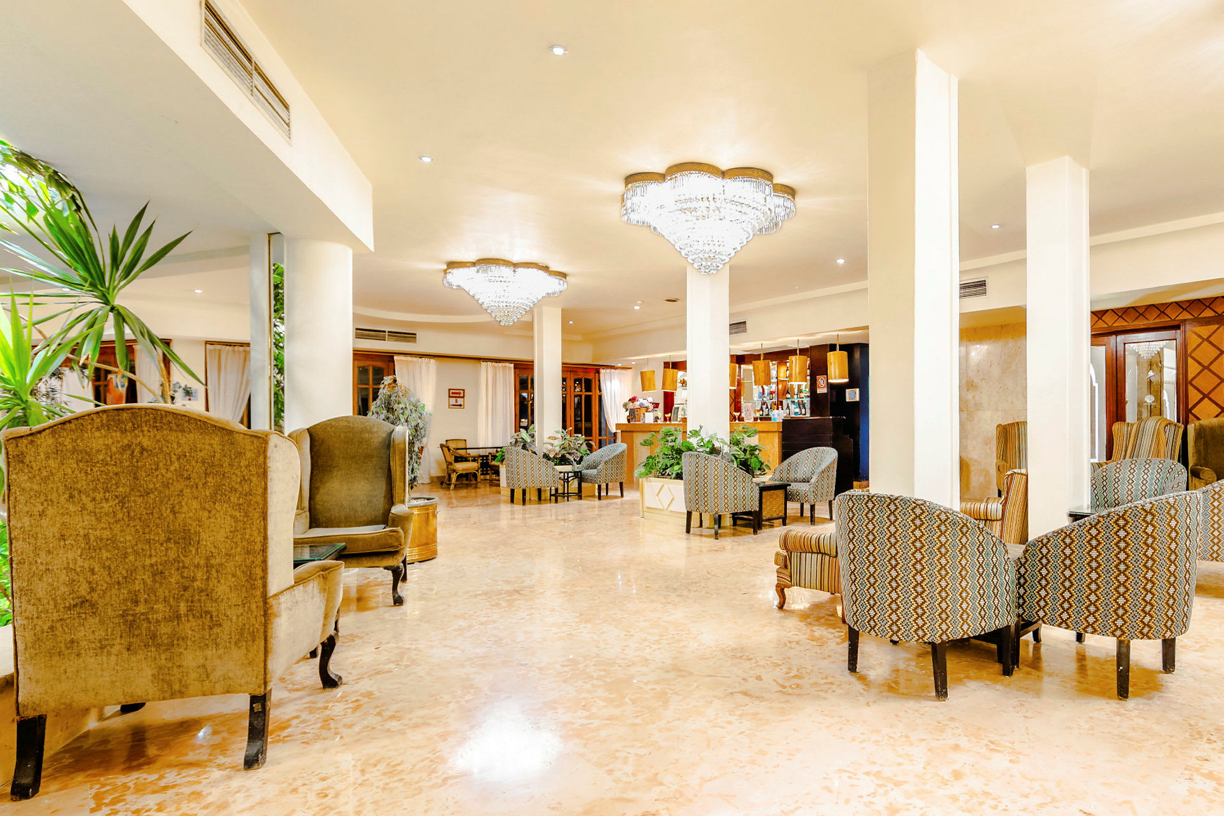 En hotellobby med sittegrupper, grønne planter og lysekroner i taket. (AI-generert tekst)