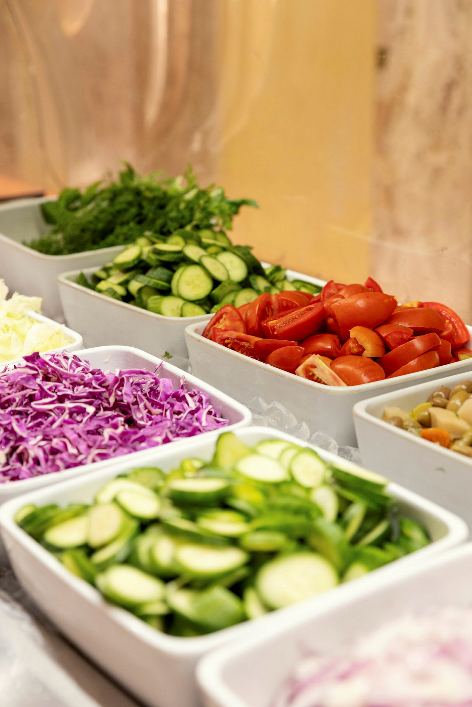 En buffet med forskjellige grønnsaker som tomater, agurk, rødkål og salat lagt opp i hvite skåler. (AI-generert tekst)