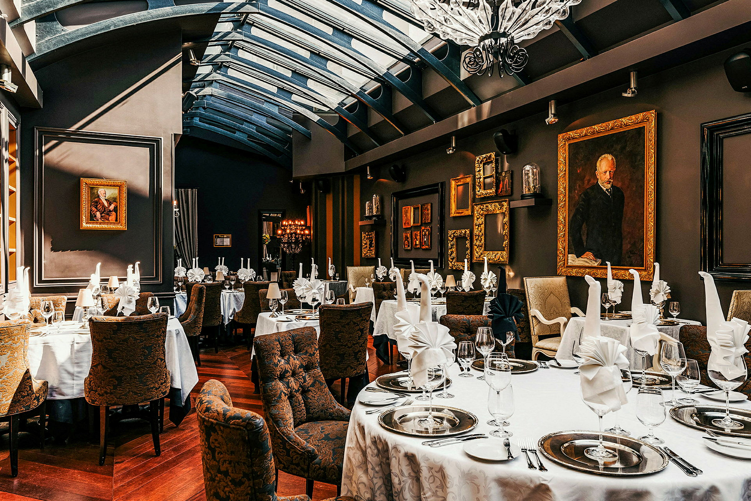 Bildet viser en elegant restaurant med dekkede bord, hvite duker, brettede servietter og dekorative tallerkener. Veggene er dekorert med kunstverk og gullrammer. (AI-generert tekst)