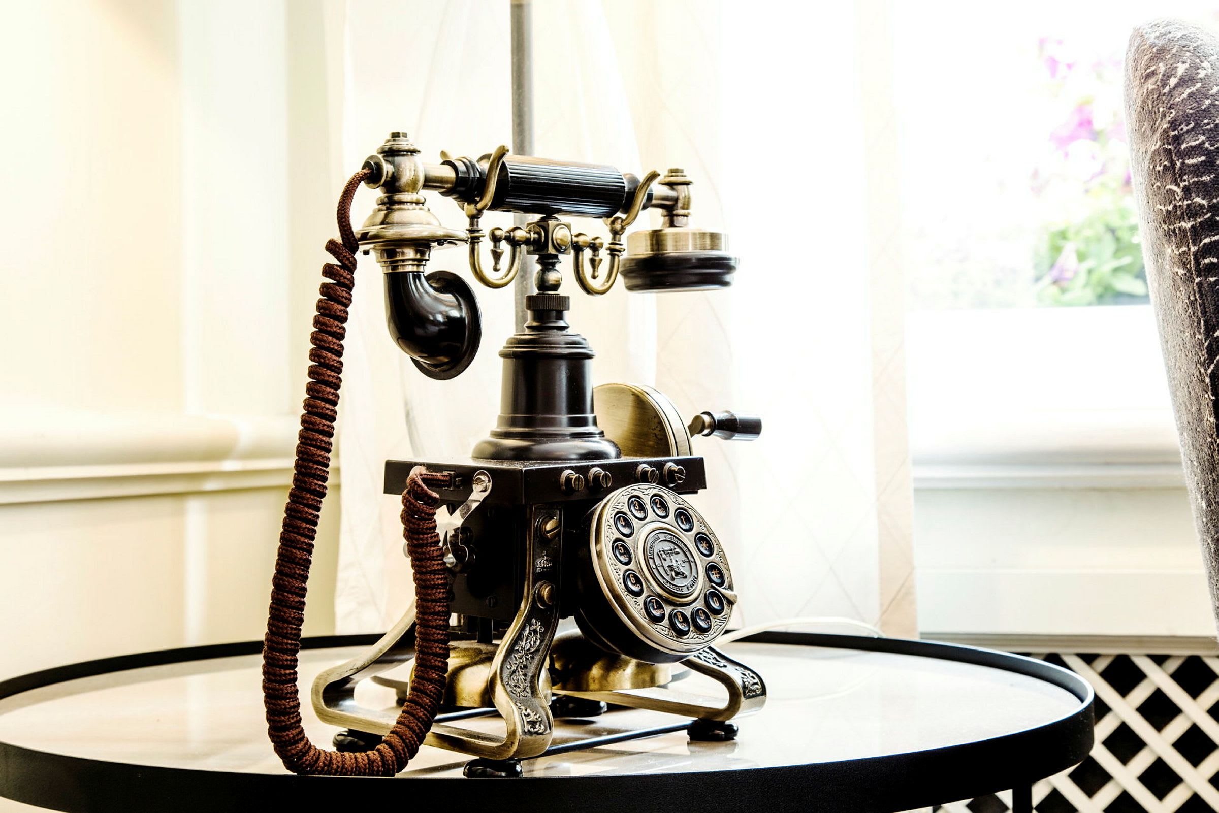Antikk telefon på et rundt bord nær et lysinnslipp. (AI-generert tekst)