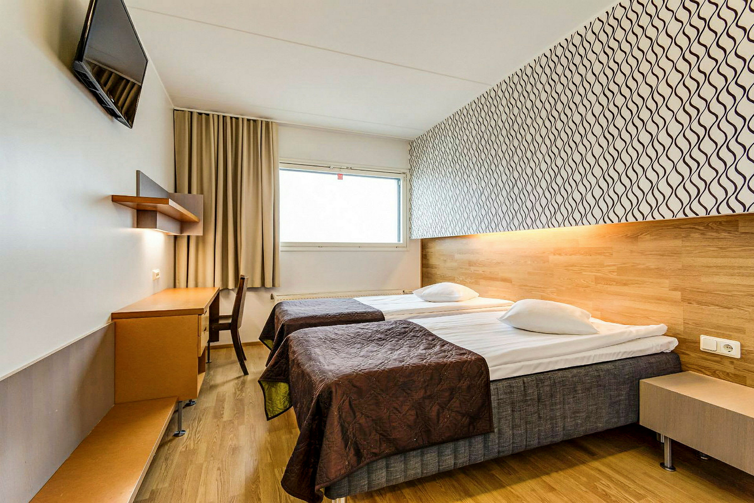 Et hotellrom med to enkeltsenger, et skrivebord og en veggmontert TV. (AI-generert tekst)