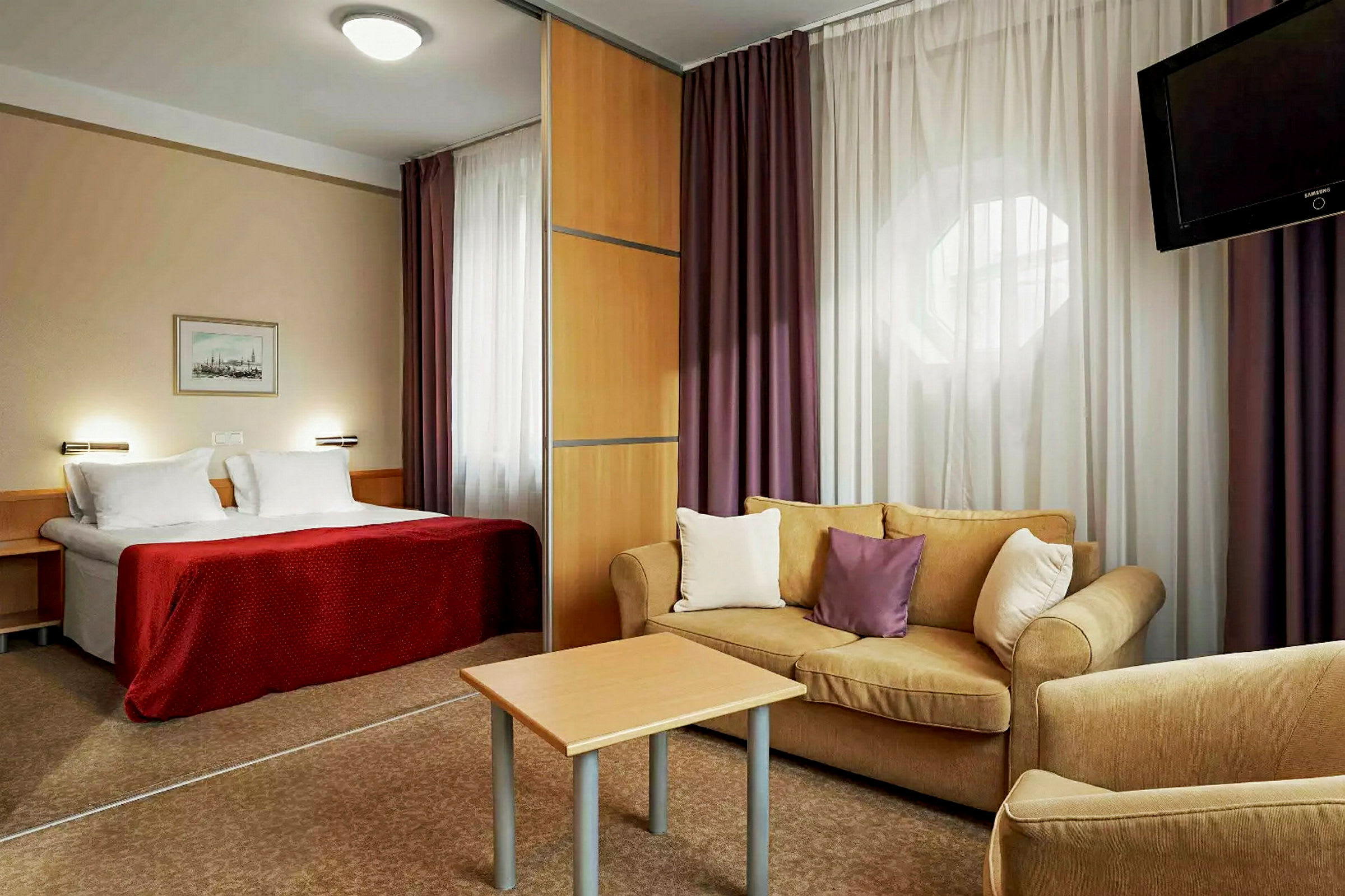 Hotellrom med en seng, en stue med sofa og et bord samt en TV. (AI-generert tekst)
