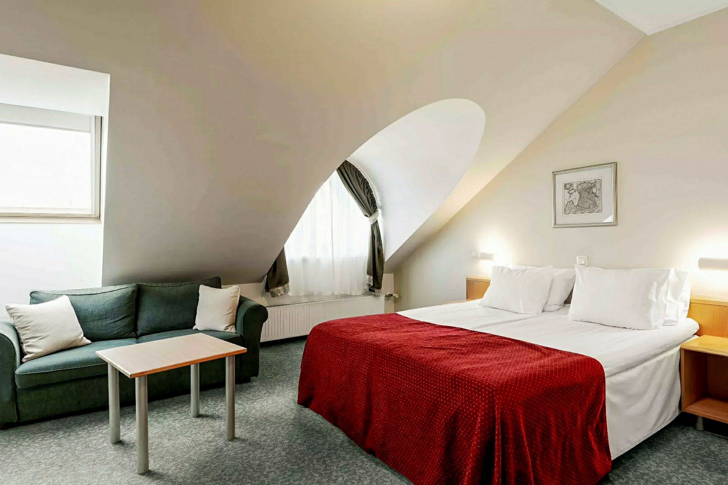 Et hotellrom med en dobbeltseng, en grønn sofa og et lite bord. (AI-generert tekst)