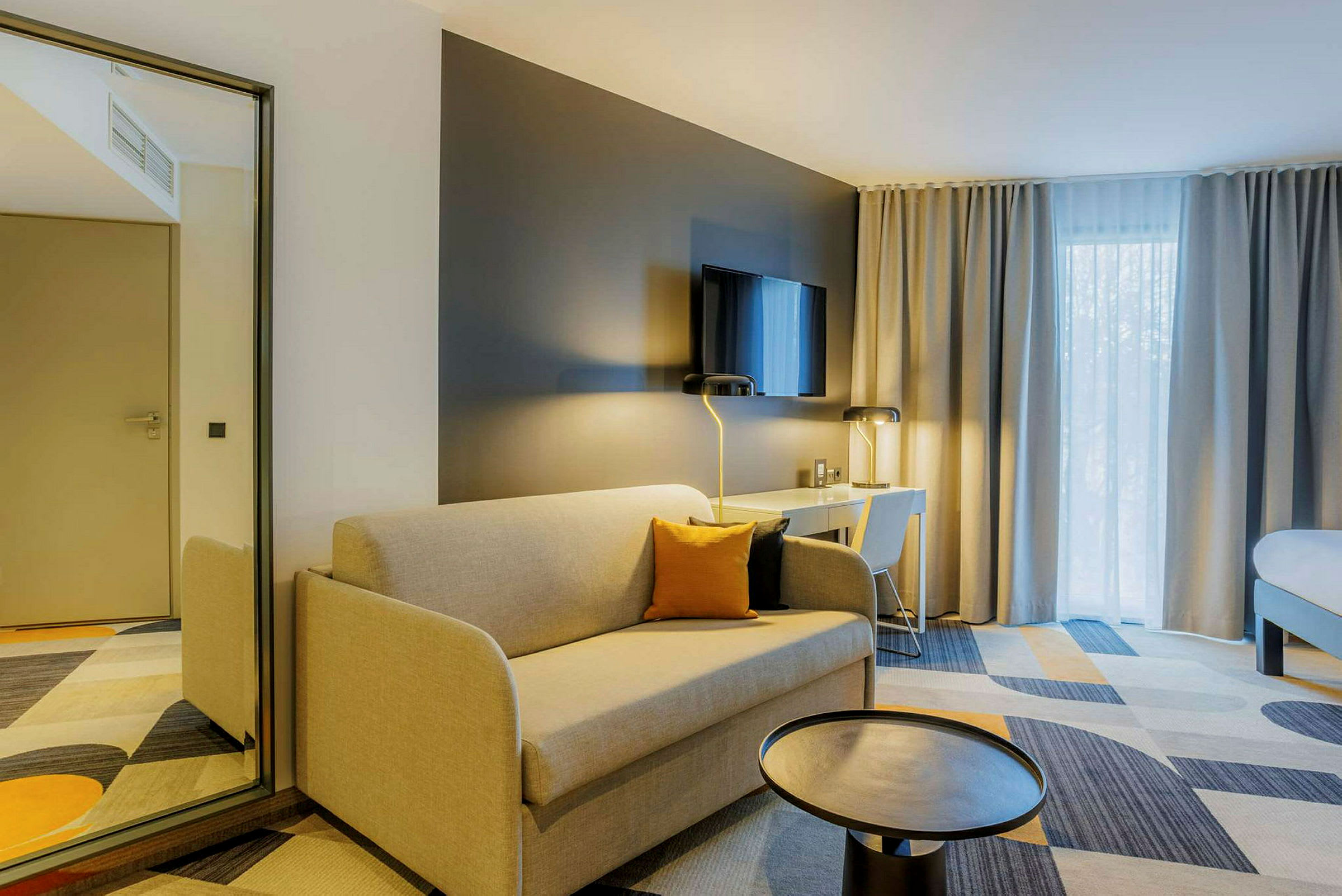 Moderne hotellrom med beige sofa, svart bord, skrivebord med stol og TV på veggen. (AI-generert tekst)