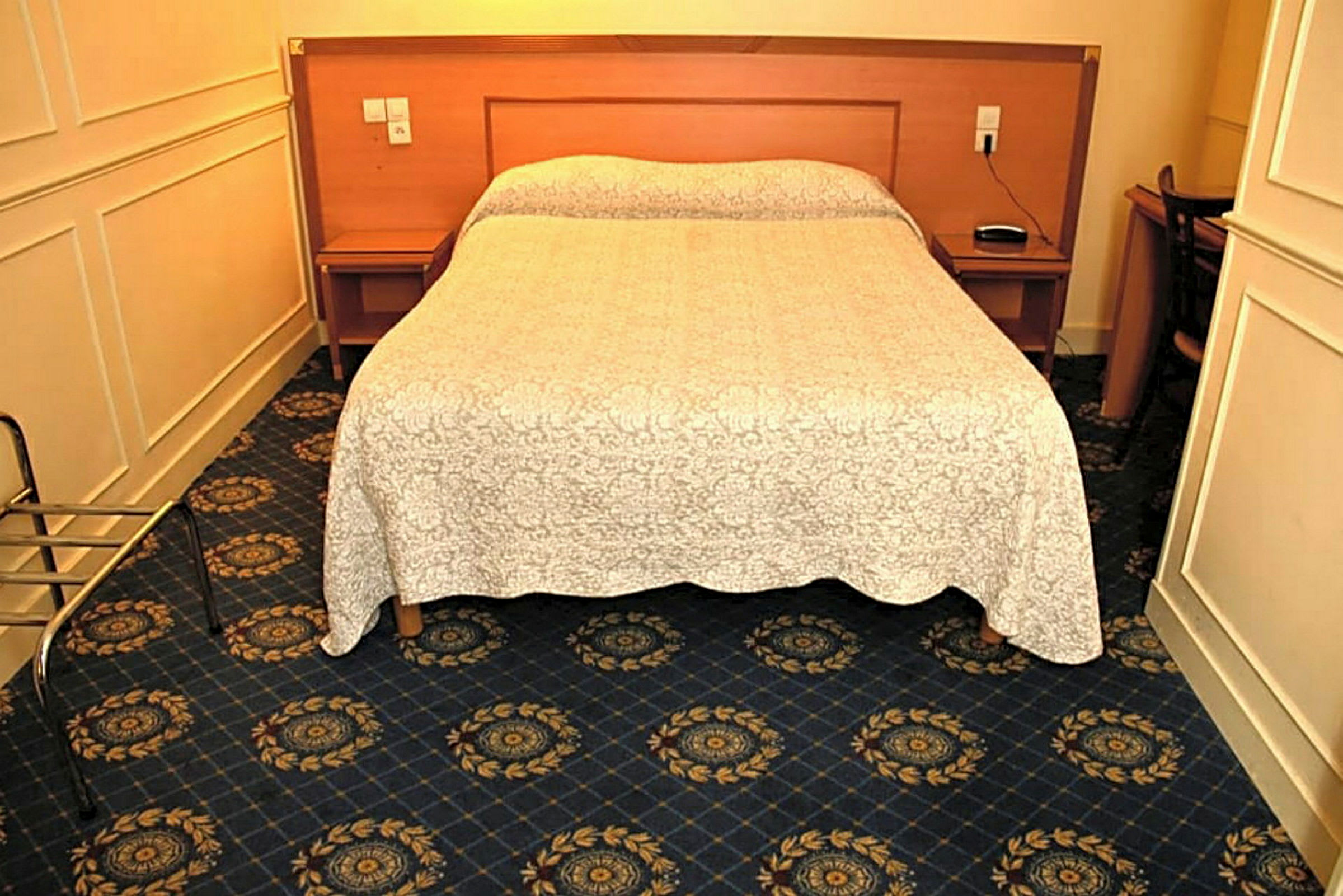 Et hotellrom med en dobbeltseng, mørkeblått teppe og et hvitt sengeteppe. (AI-generert tekst)