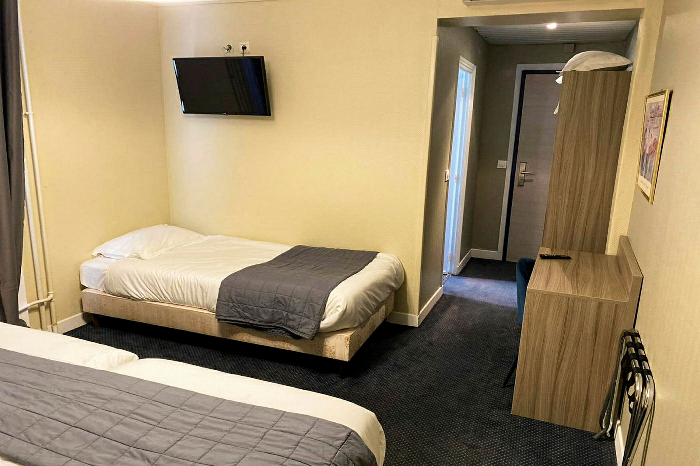 Et hotellrom med to enkeltsenger, en veggmontert TV og møbler. (AI-generert tekst)