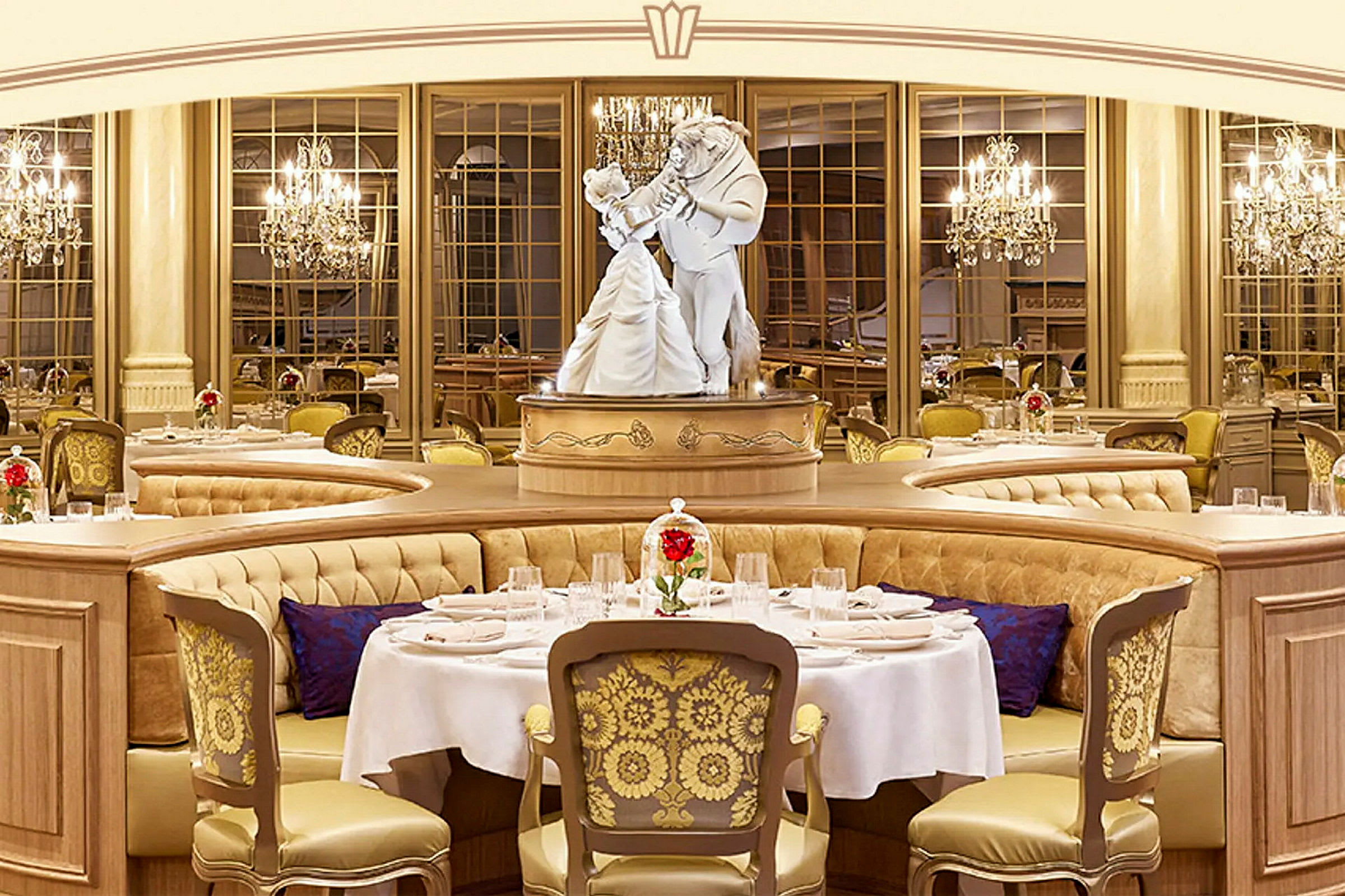 Et bilde av en elegant restaurant med luksuriøse møbler og en statue som viser to dansende figurer i sentrum. Bordene er dekorert med hvite duker og røde blomster i glasskupler. (AI-generert tekst)