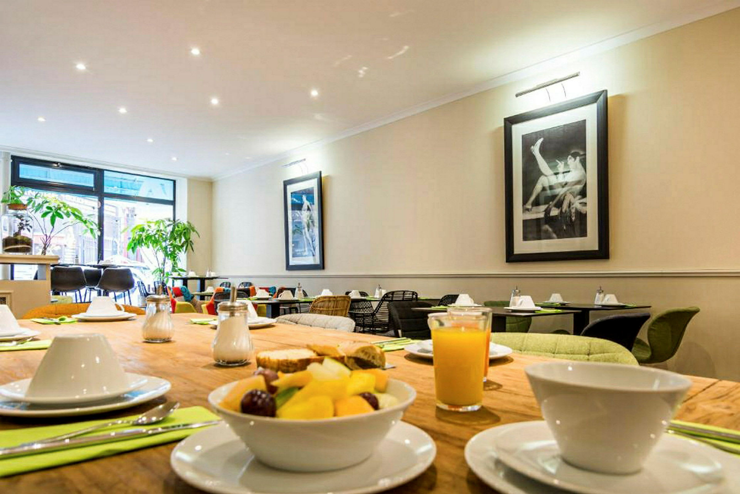 Et dekket bord med frokost, med juice og fruktsalat samt en spisesal i bakgrunnen. (AI-generert tekst)