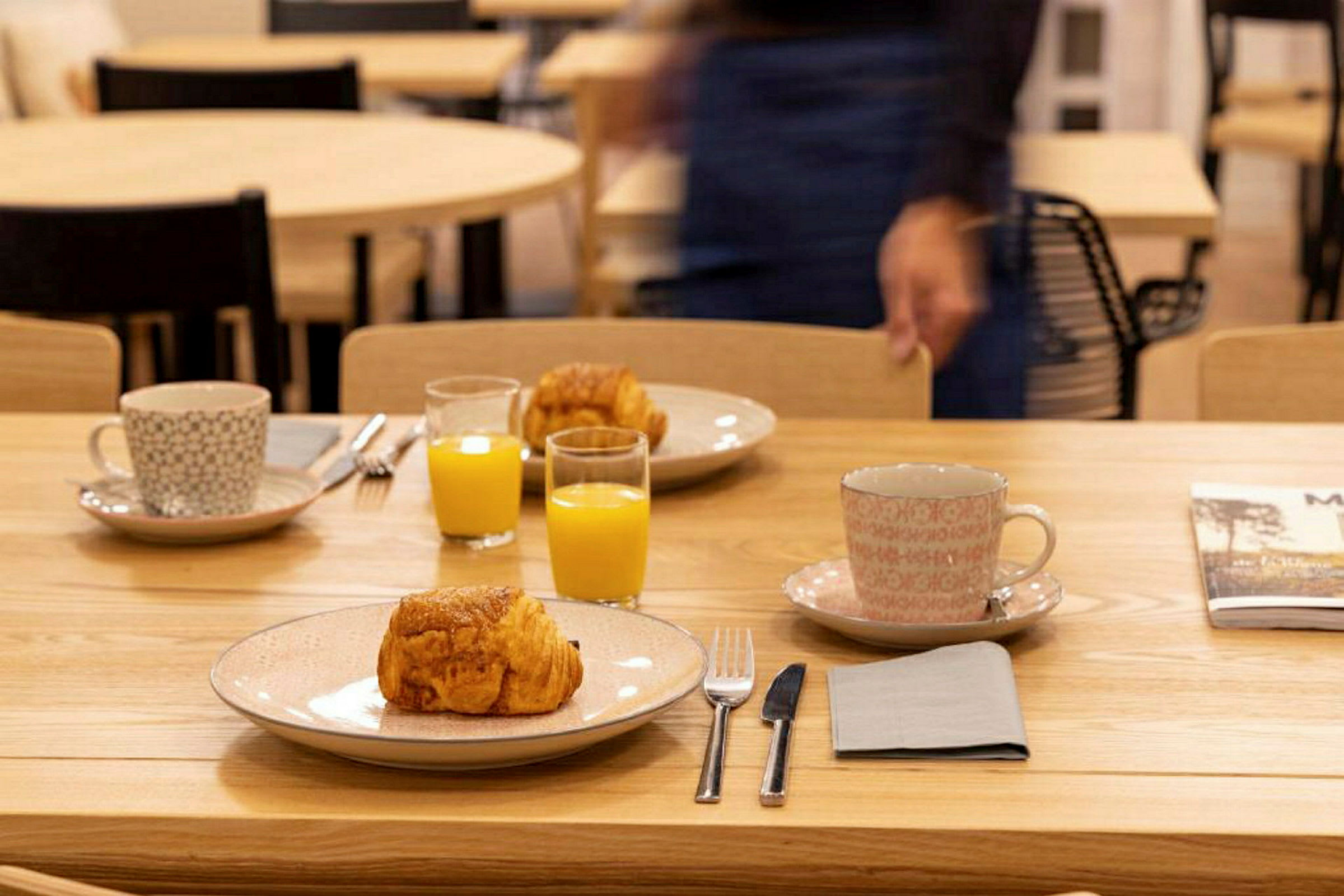 Et bord dekket med tallerkener, croissanter, kopper og glass med appelsinjuice. (AI-generert tekst)