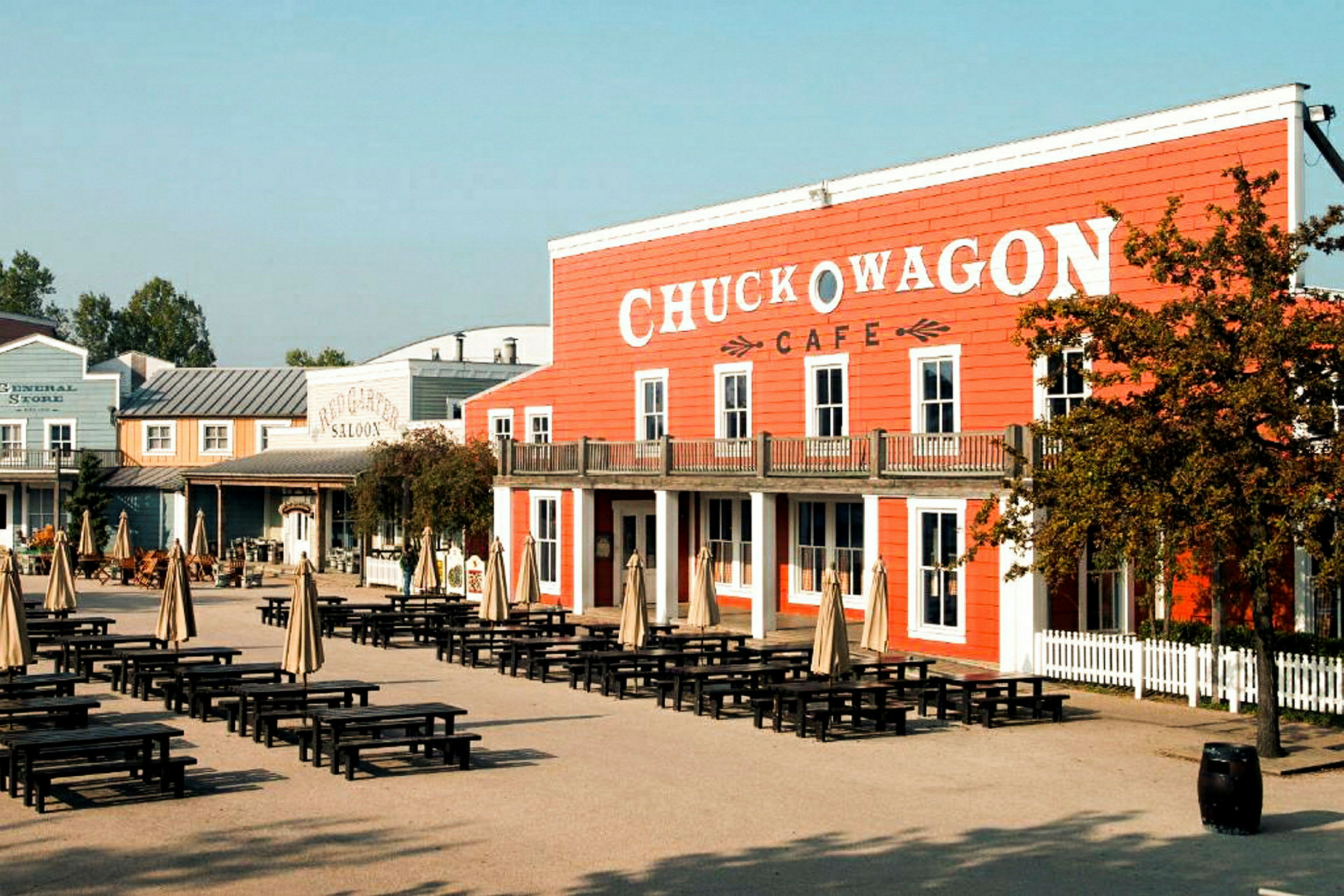 Et område med bord og parasoller foran en bygning med skiltet 'Chuck Wagon Cafe'. (AI-generert tekst)