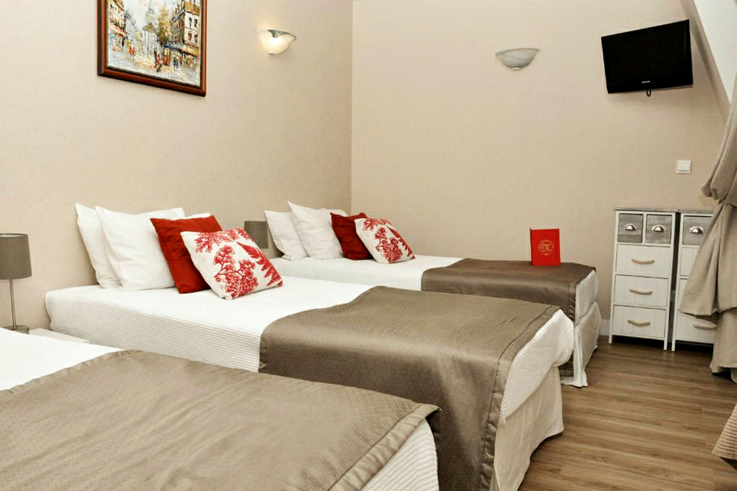 Hotellrom med tre enkeltsenger, dekorert med røde og hvite puter. (AI-generert tekst)