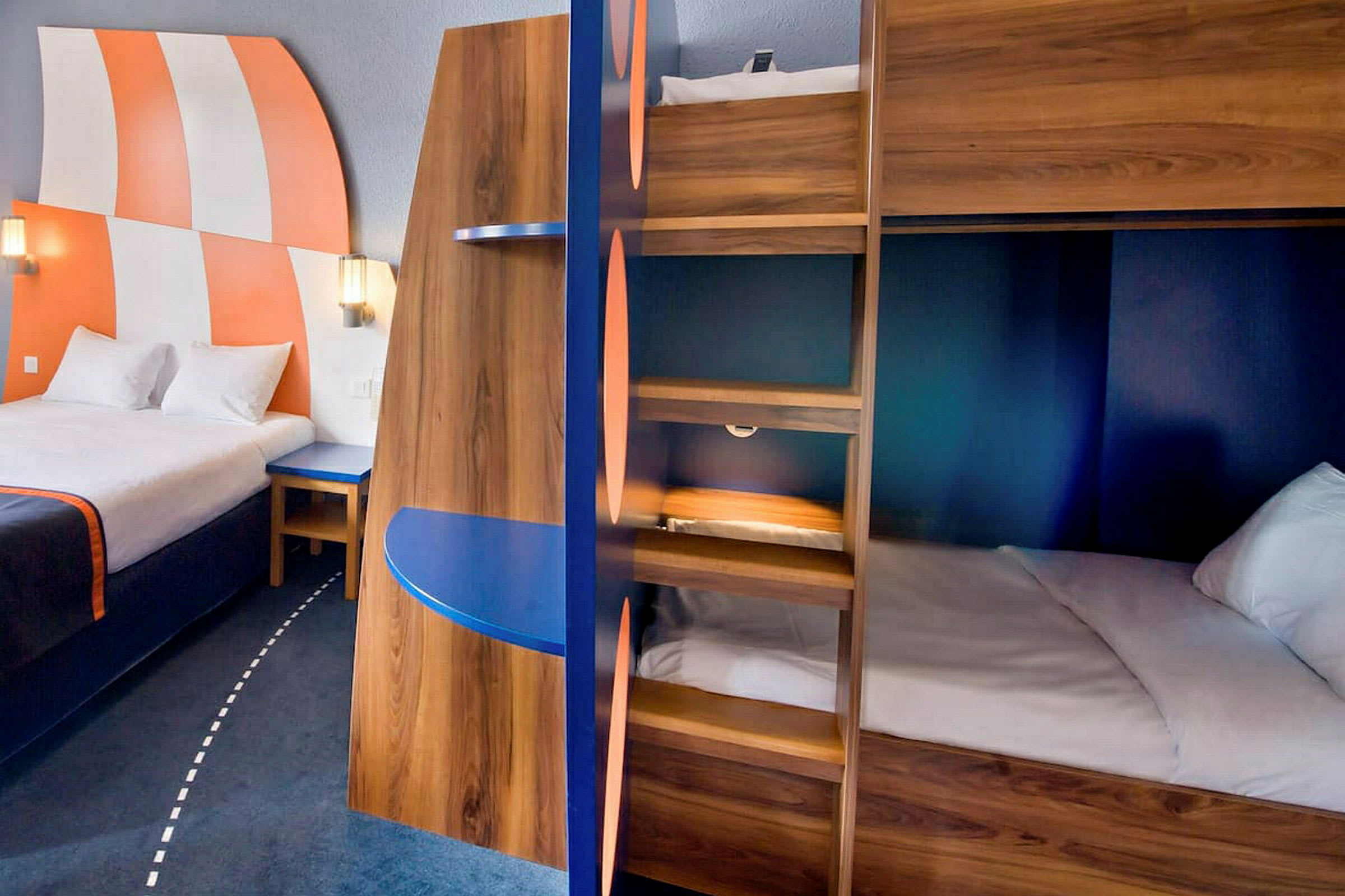 Interiør av et hotellrom med en stor seng, køyesenger og fargerike detaljer. (AI-generert tekst)