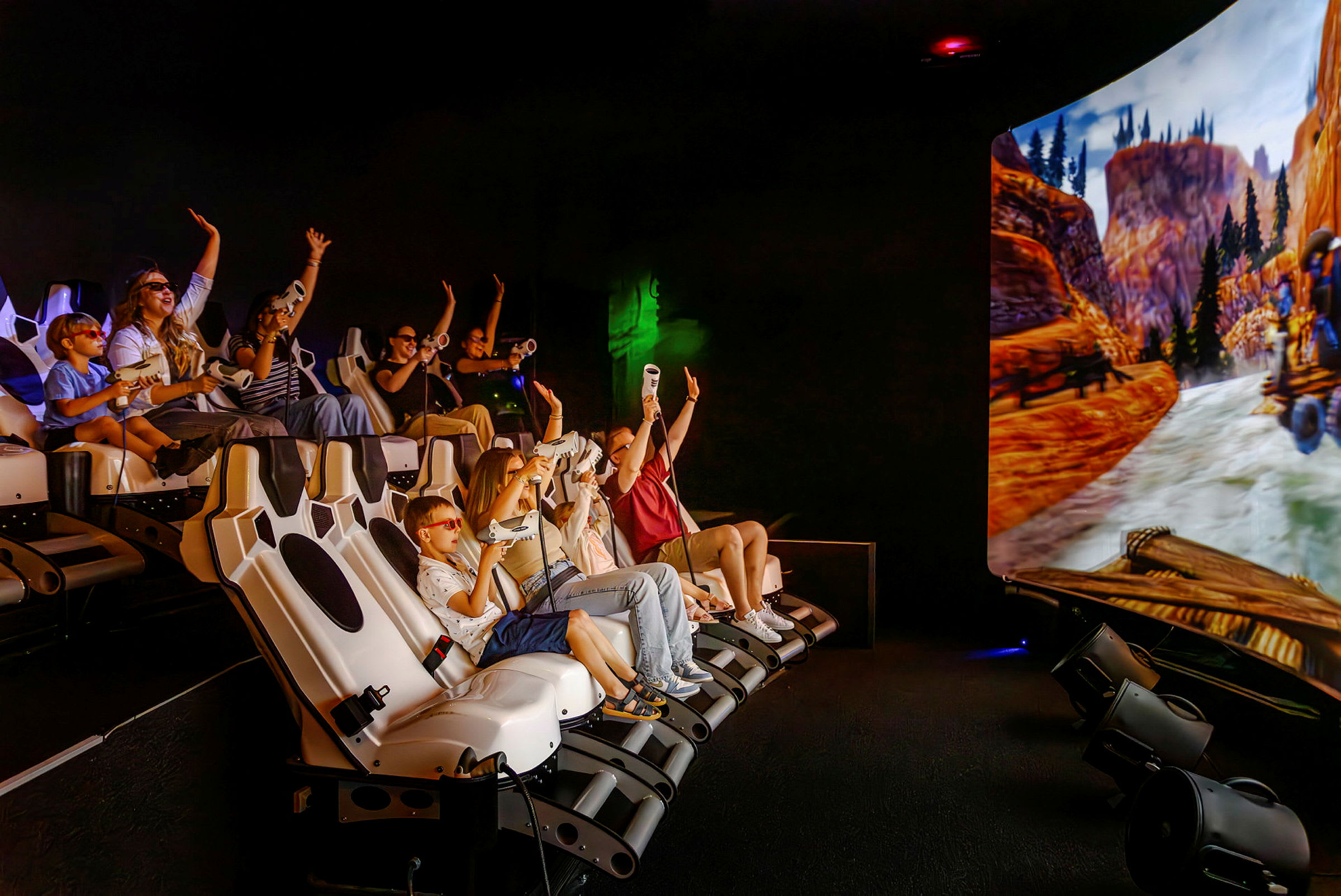 En gruppe mennesker sitter i en interaktiv simulator med en stor skjerm som viser en naturscene med fjell og elv. (AI-generert tekst)