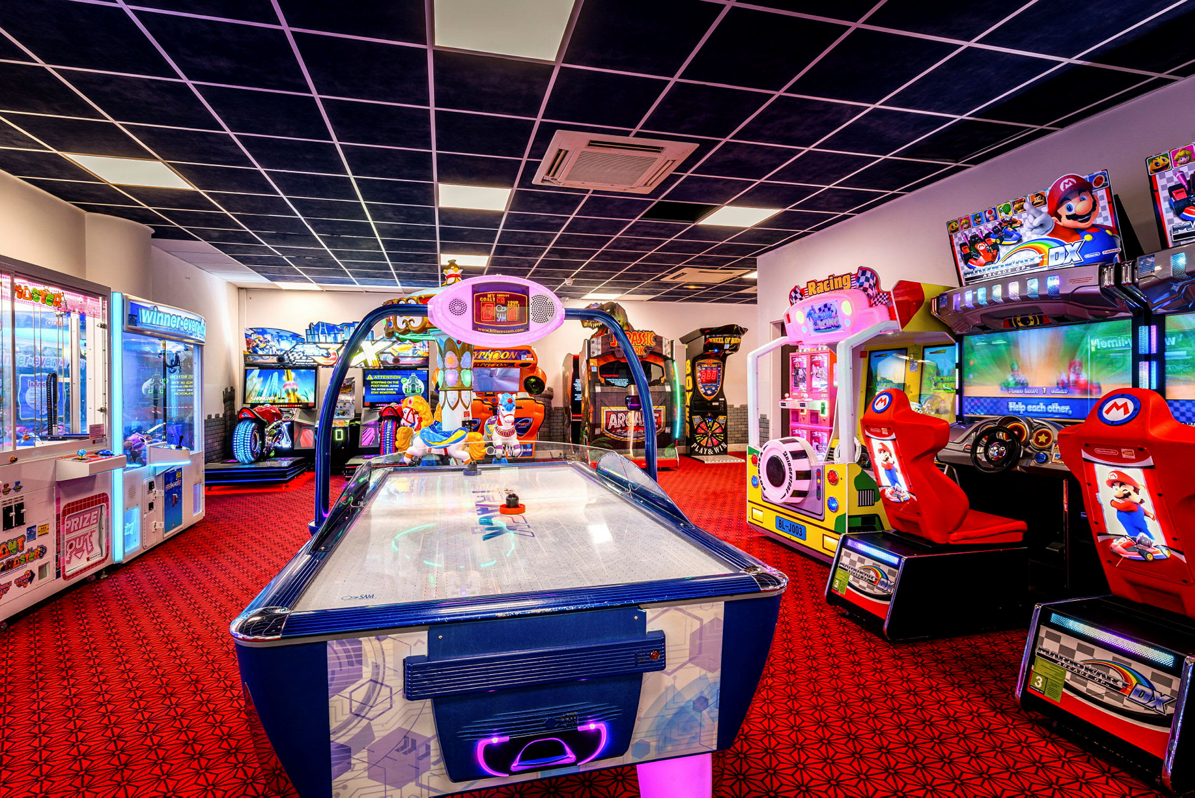 Et bilde av et spillearkaderom med forskjellige spillmaskiner og en airhockey-maskin i forgrunnen. (AI-generert tekst)