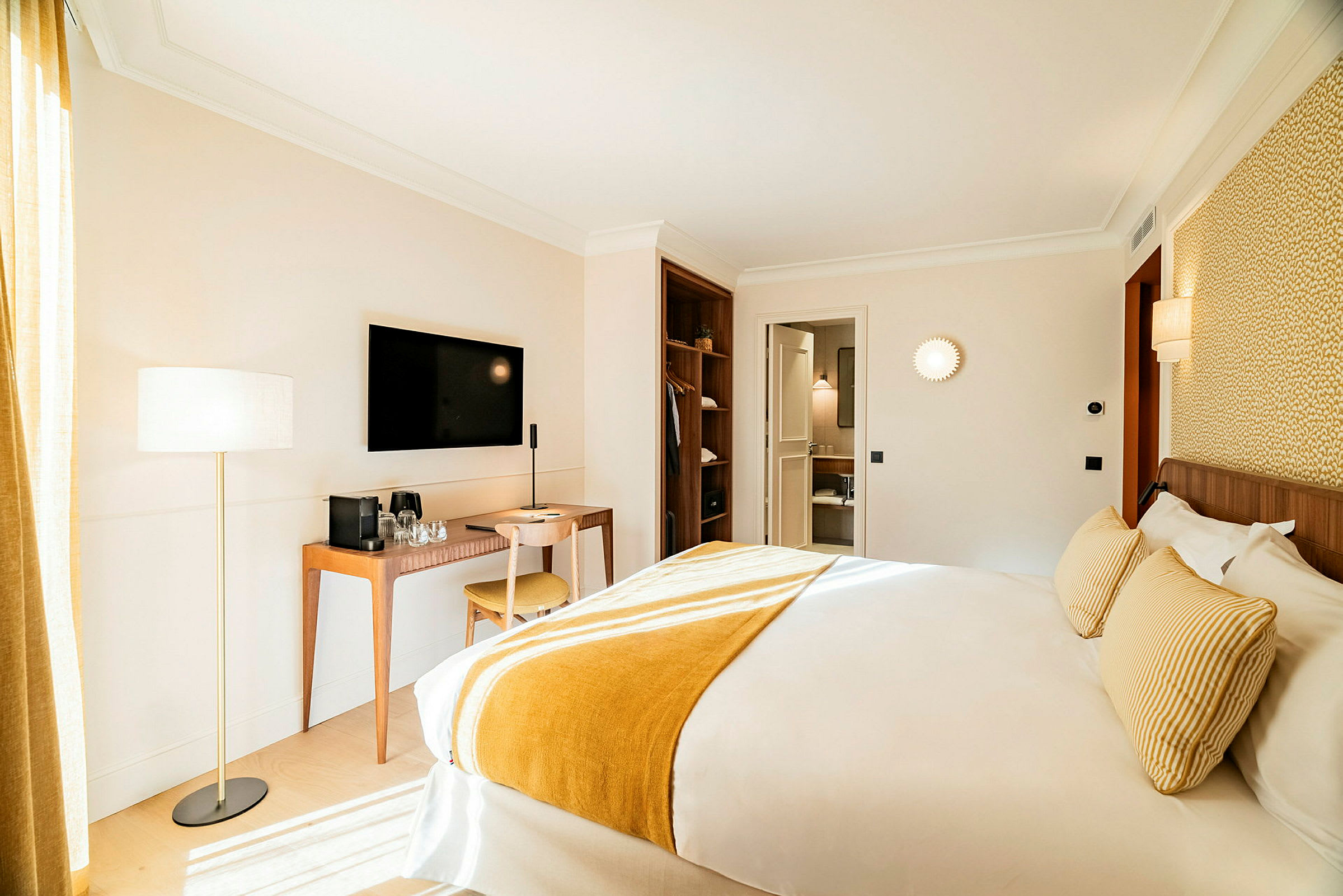 Et hotellrom med en stor seng, skrivebord og stol samt en veggmontert TV. Rommet er lyst innredet. (AI-generert tekst)
