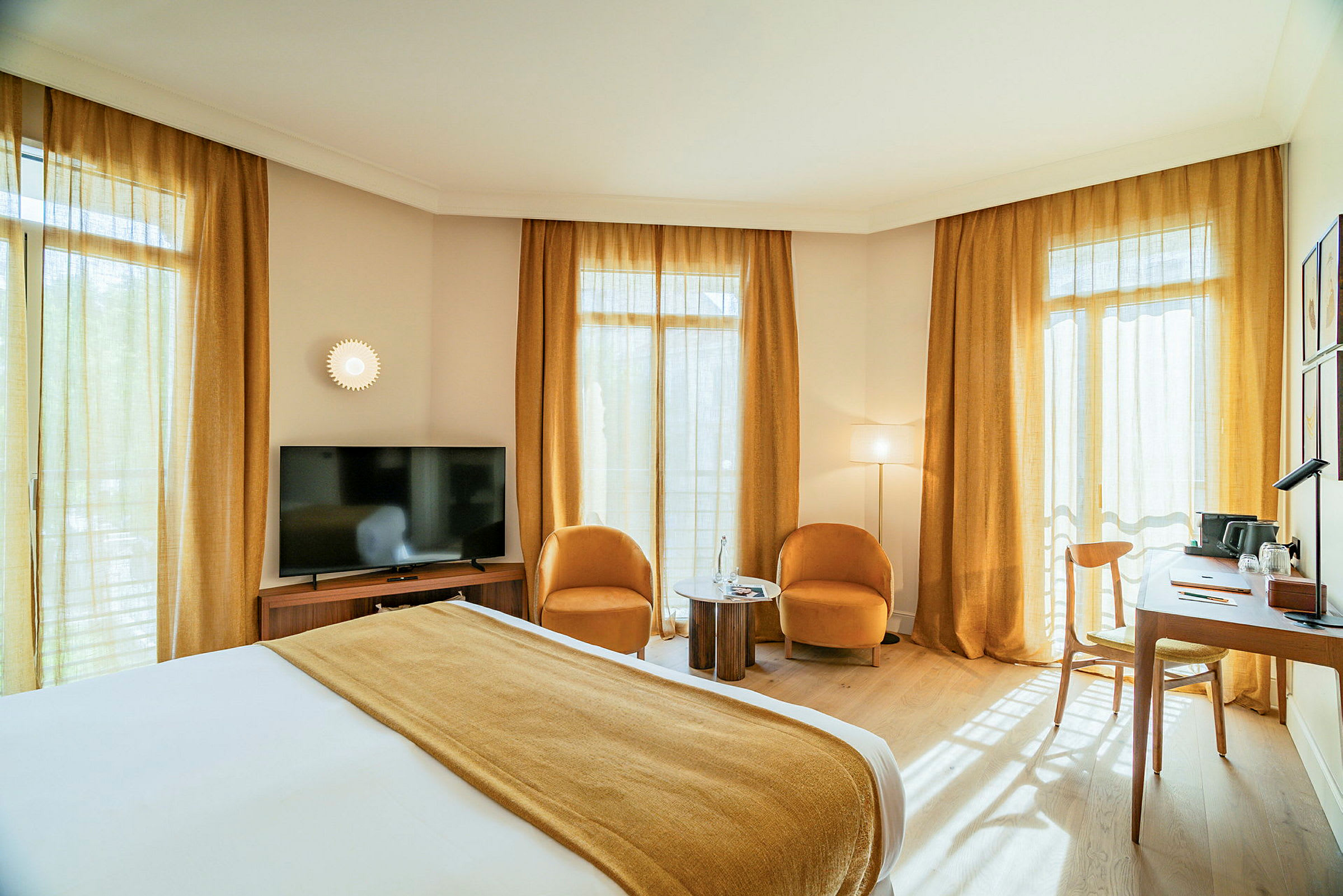 Et hotellrom med en dobbeltseng, to lenestoler og et lite bord, en TV og et skrivebord ved vinduene. (AI-generert tekst)