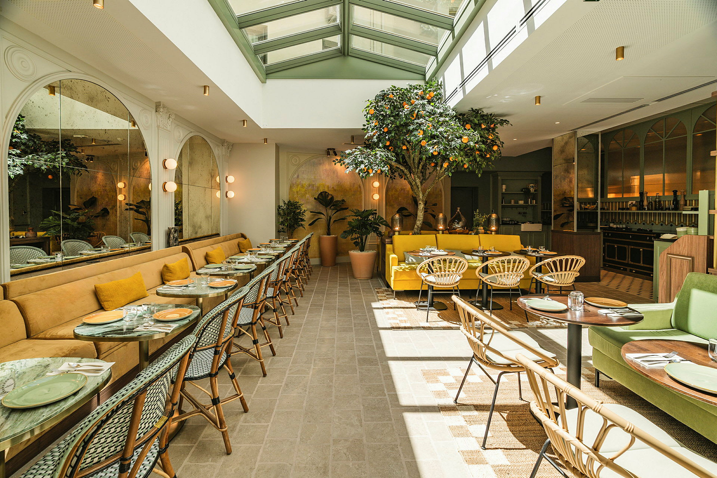 En lys og elegant restaurant med sitteplasser ved bord og sofaer. Dekorasjoner inkluderer et sitrustre og grønne planter. (AI-generert tekst)