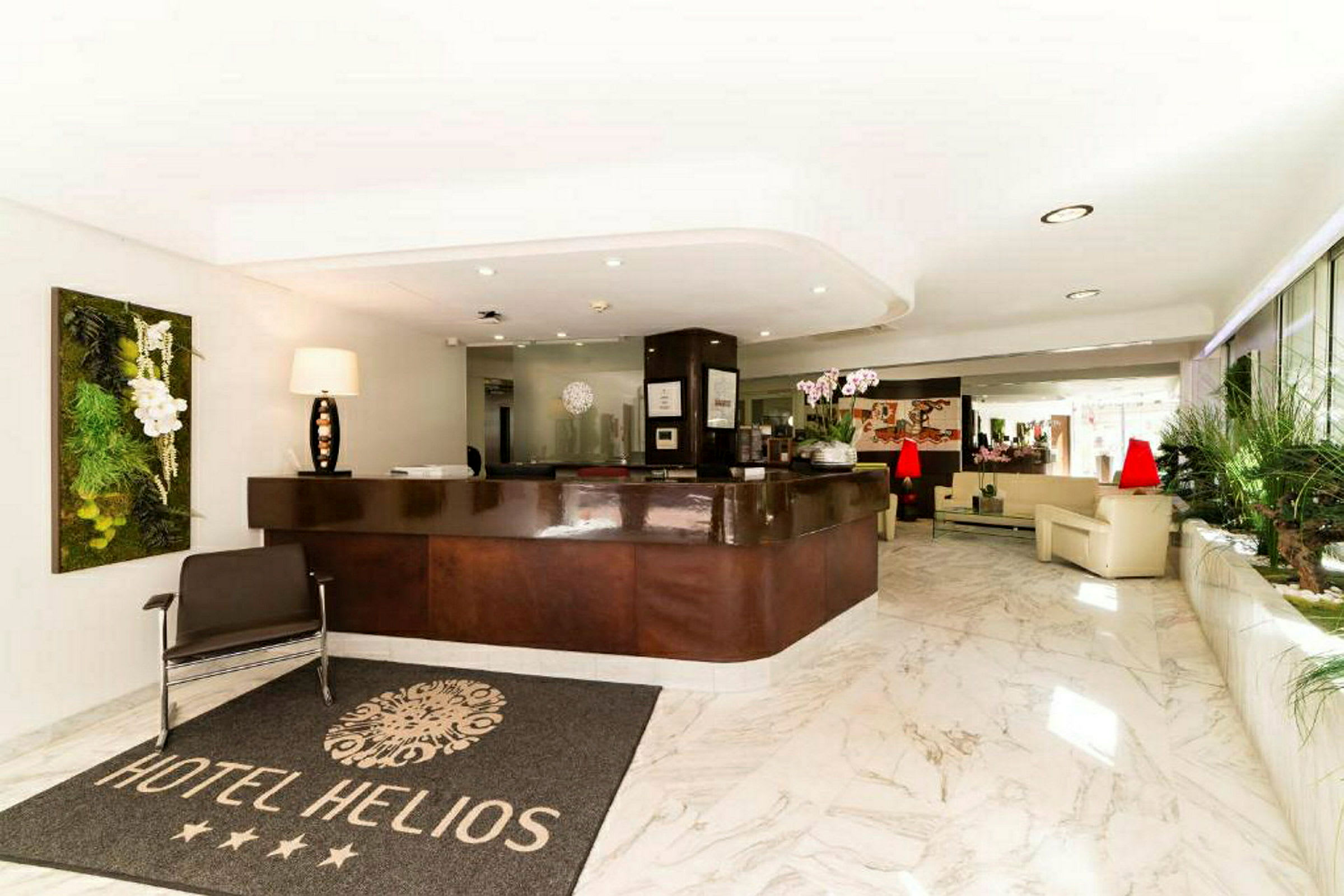 Hotellobby med resepsjon, et teppe med teksten "Hotel Helios" og sittemøbler i lyse omgivelser. (AI-generert tekst)