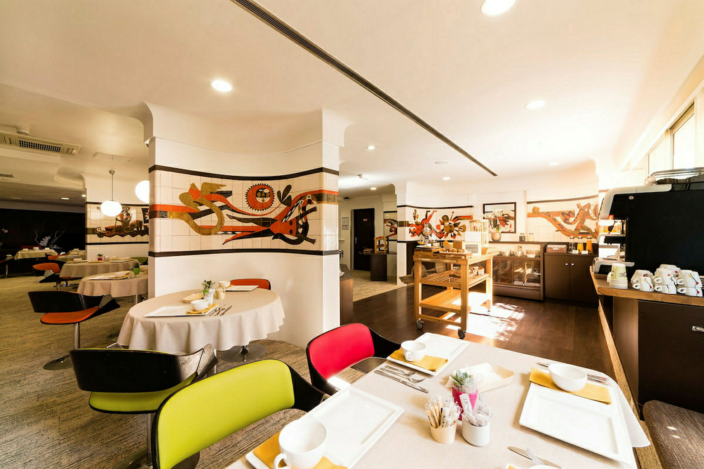 En restaurant med dekkede bord, kunst på veggene og en serveringsstasjon. Lyset er varmt og innbydende. (AI-generert tekst)