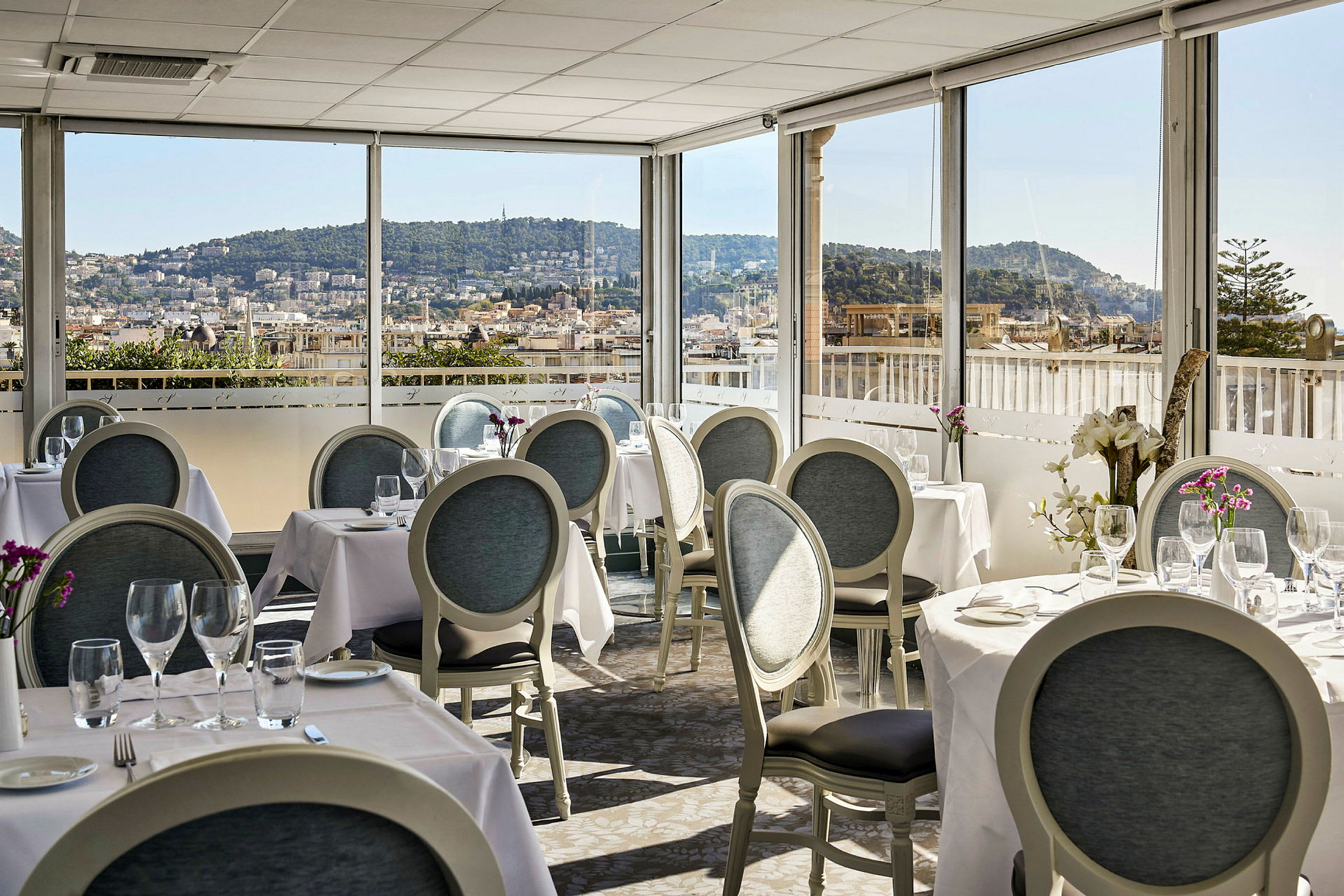 Restaurant med dekkede bord og utsikt over en by med åser i bakgrunnen. (AI-generert tekst)