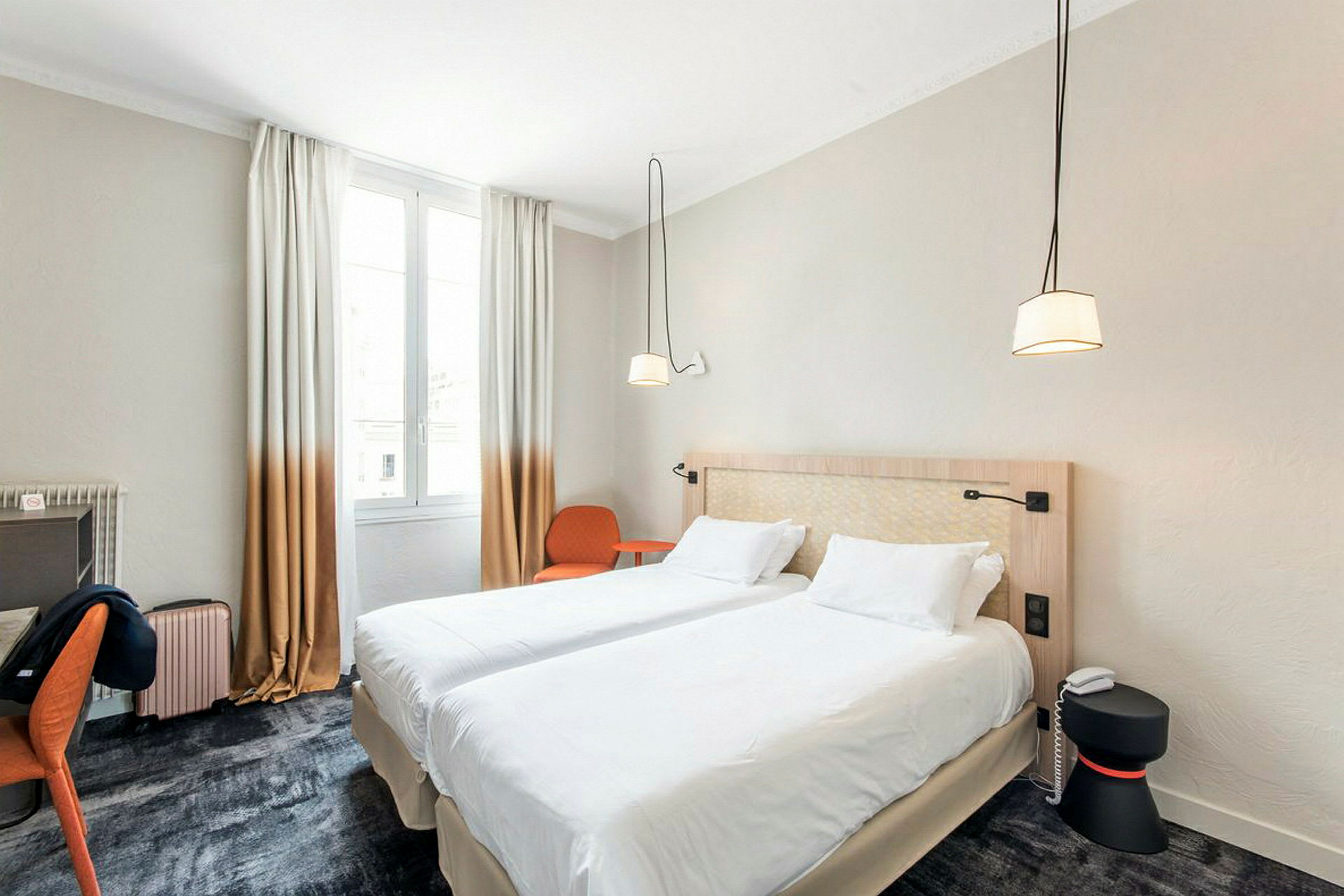 Et hotellrom med to enkeltsenger koblet sammen, et skrivebord, en stol og et lysinnslippende vindu. (AI-generert tekst)