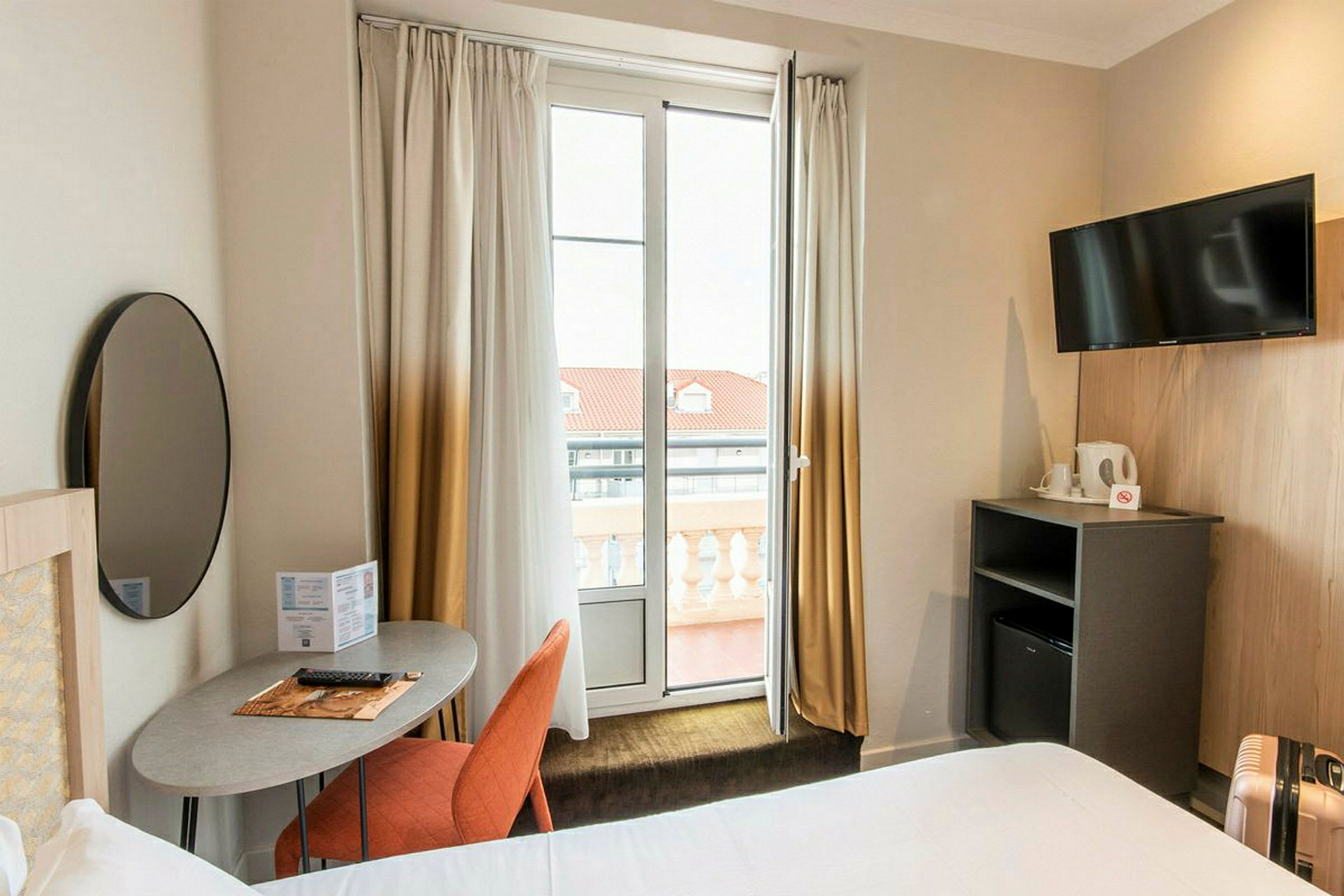 Et hotellrom med moderne innredning, inkludert et skrivebord, en stol, en TV og en balkong. (AI-generert tekst)