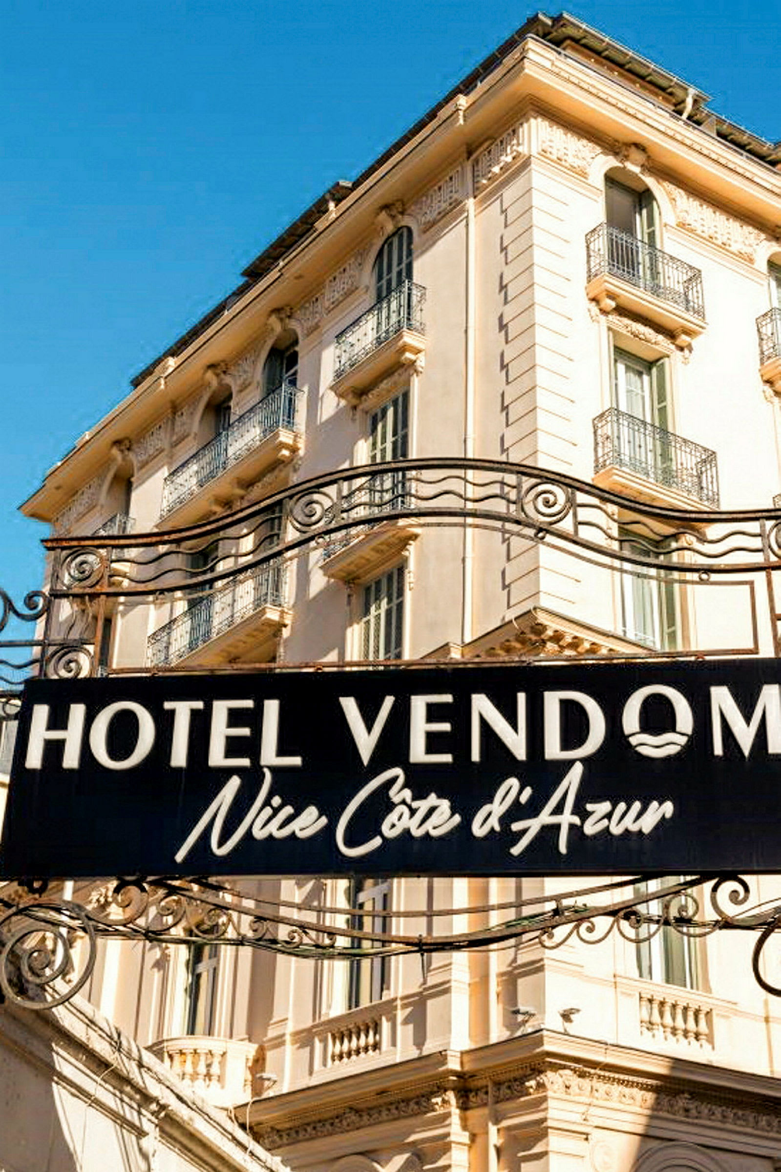 Skilt med teksten Hotel Vendome Nice Côte d’Azur foran en beige bygning. (AI-generert tekst)