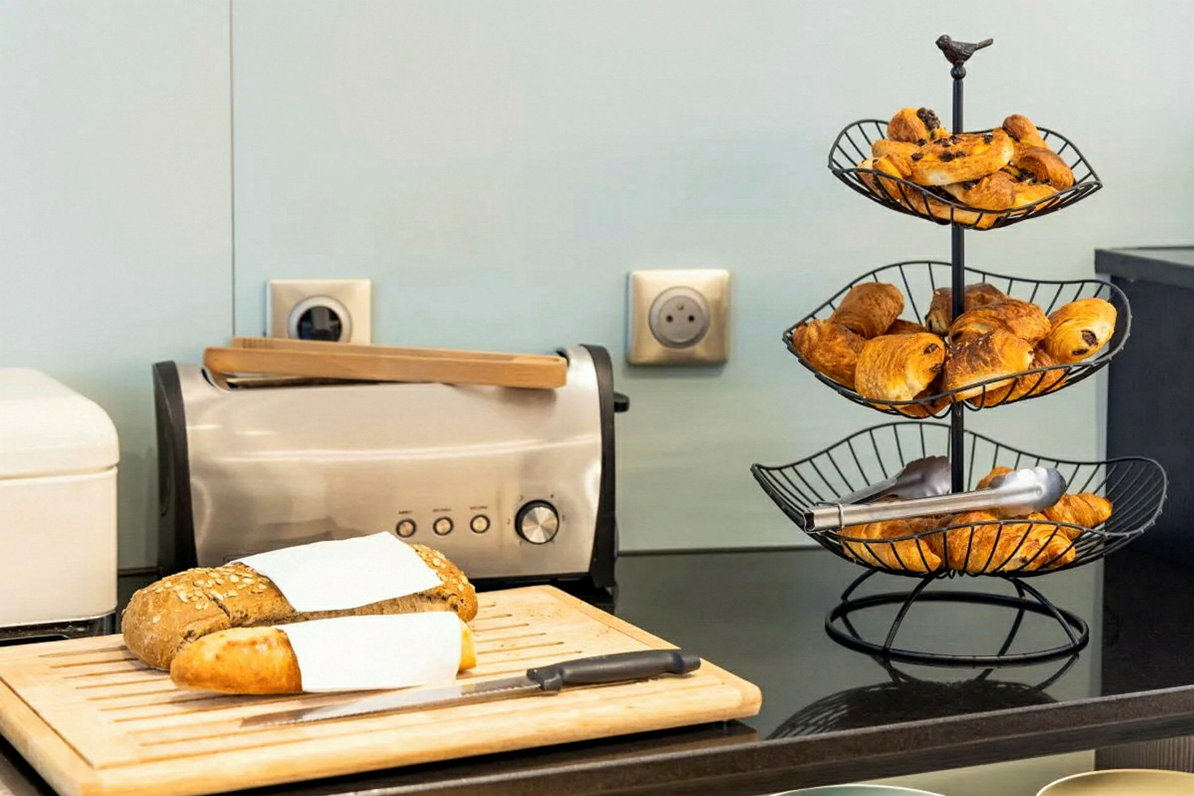 Bilde av et brødfat med en brødrister og et brødstativ med croissanter på en kjøkkenbenk. (AI-generert tekst)